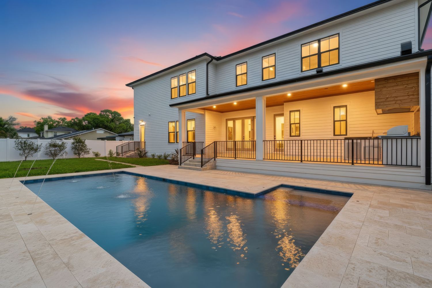 Luxurious modern home exterior with infinity pool reflecting dramatic sunset sky and warm interior lighting.