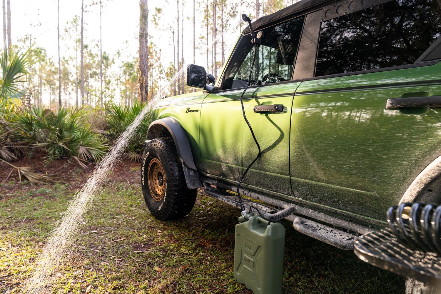 Green off-road vehicle driving through a wooded trail with tall pine trees.
