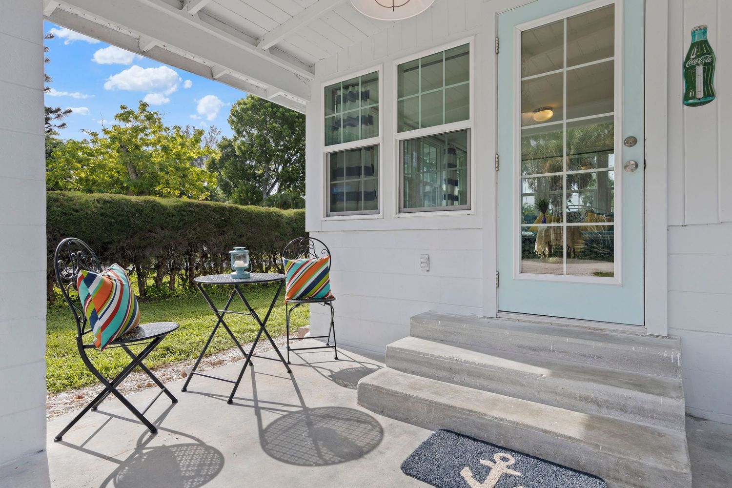 A bright white coastal home features multiple covered porches with black rocking chairs and outdoor seating areas.