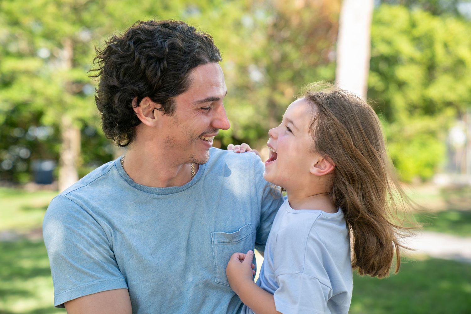 A couple shares a tender moment together while laughing and embracing outdoors in a sunny garden setting.
