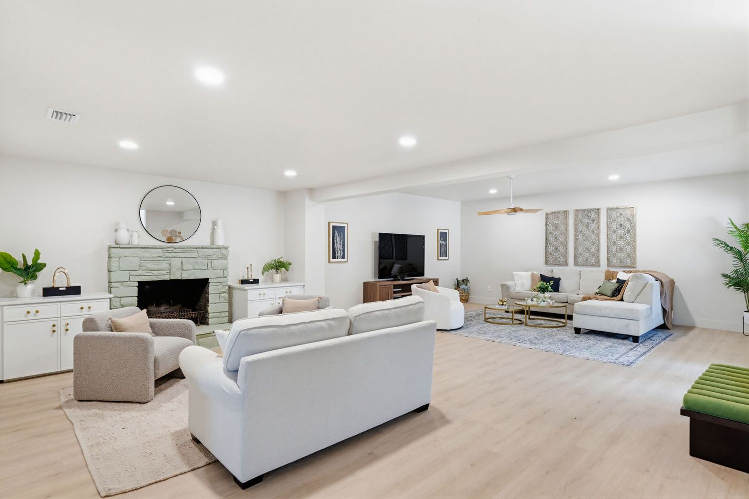 Modern white living room interior with recessed lighting, gray sectional sofa, and minimalist decor in a bright open space.