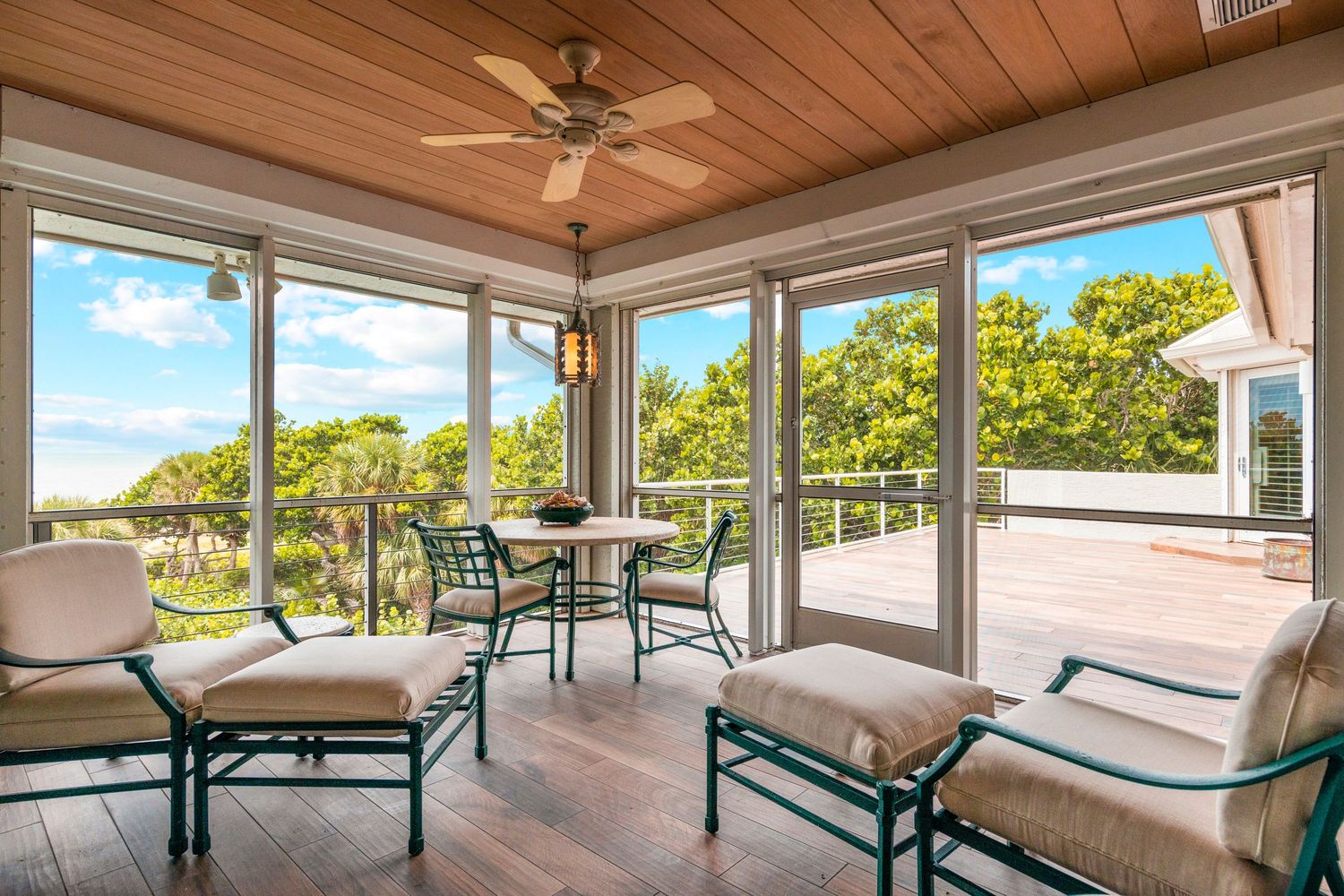 Bright sunroom with wooden ceiling, comfortable seating, and large windows overlooking lush outdoor views.