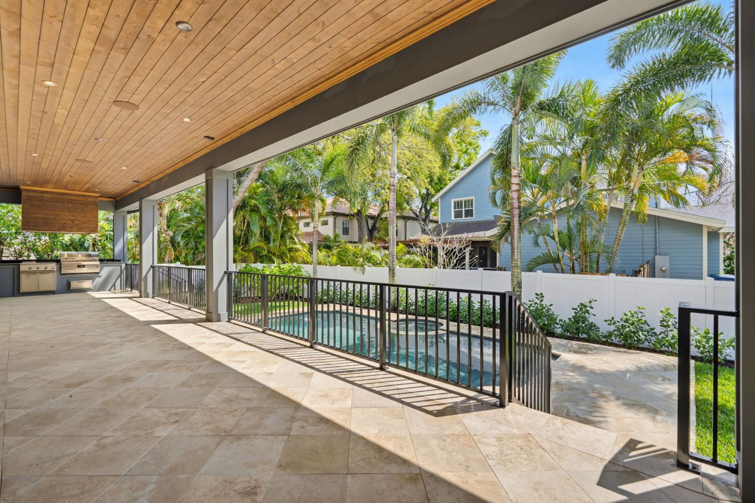 Modern covered patio with wood ceiling, metal railings and tropical palm trees in the background.