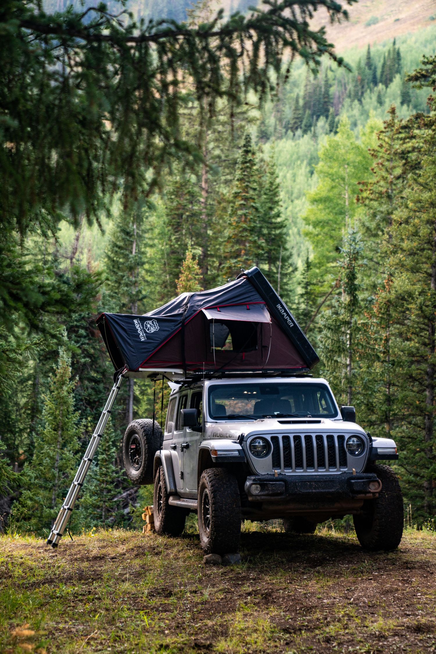 Jeep Wrangler with rooftop camping tent in scenic mountain forest landscape.