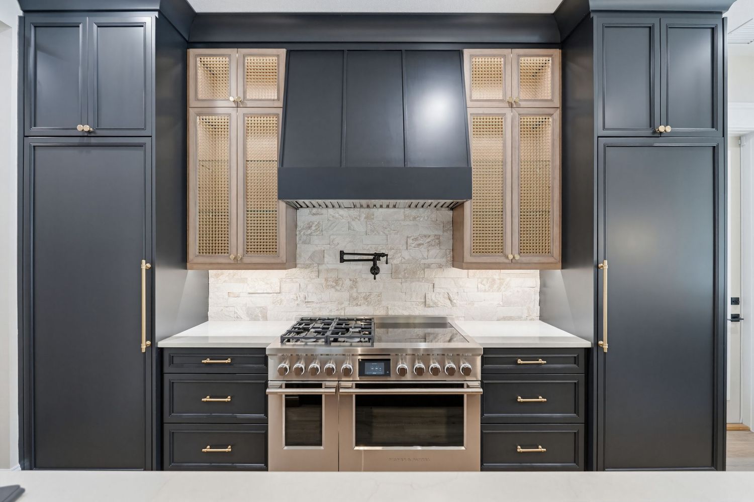Modern kitchen design with dark blue cabinets, gold hardware, and glass-front upper cabinets featuring wood interior panels.