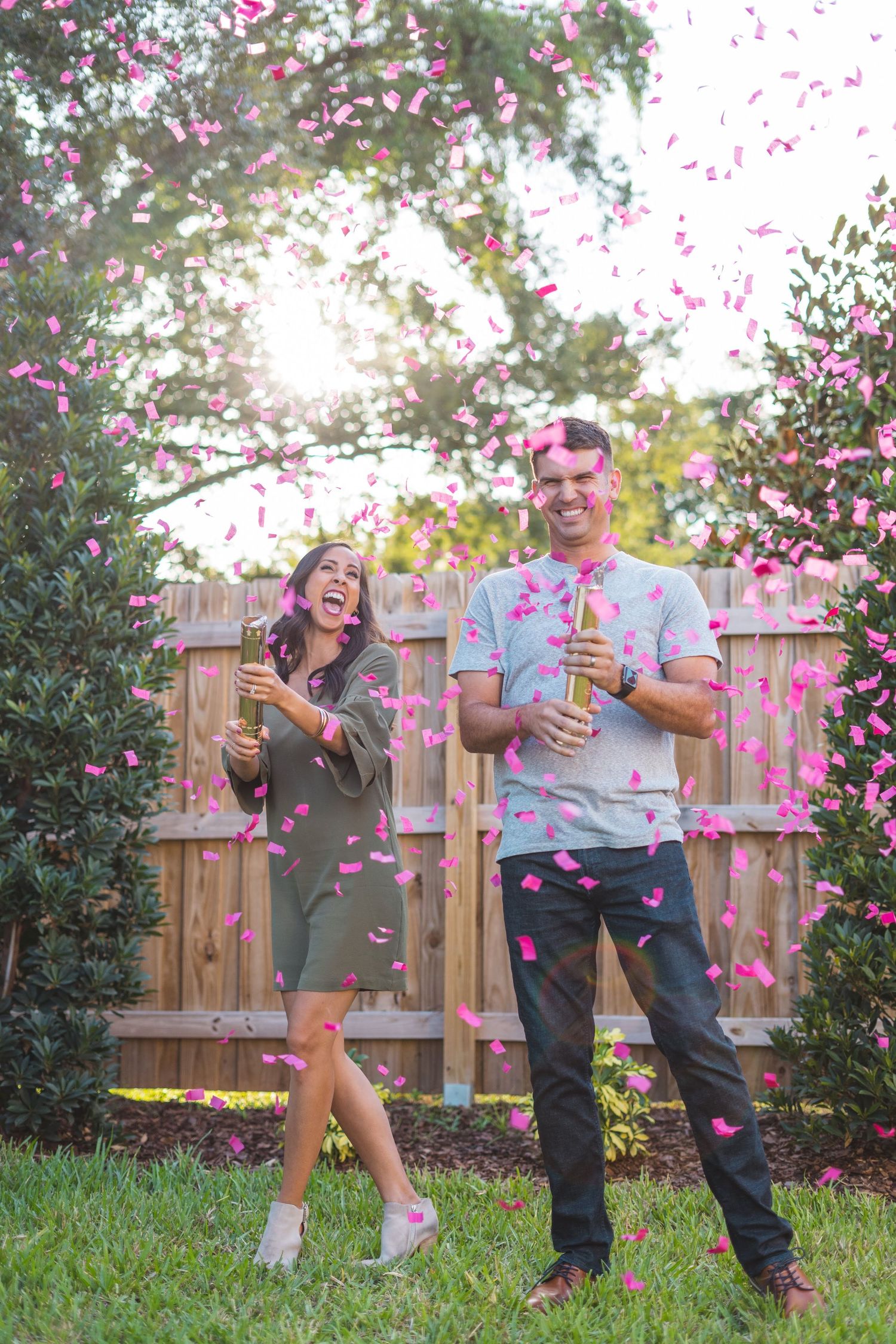 Couple celebrating with pink confetti falling in their backyard during golden hour.