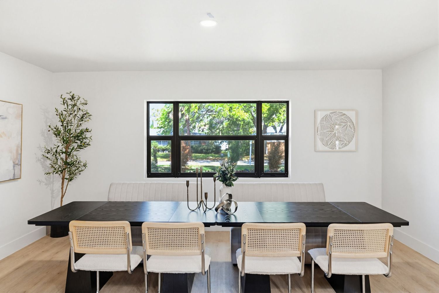 Modern white dining room with black dining table, white chairs, and transom windows letting in natural light.