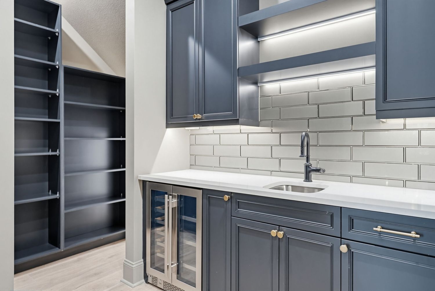 Modern laundry room features navy blue cabinets, white subway tile backsplash, and stainless steel appliances.