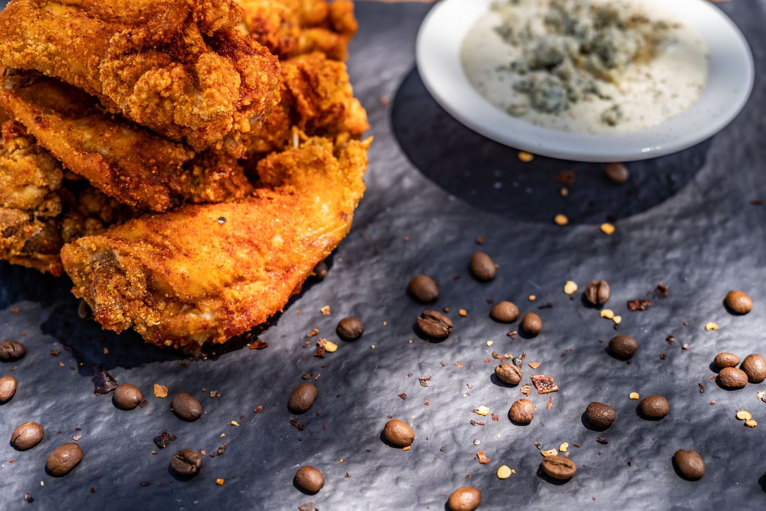 Crispy fried chicken pieces with scattered coffee beans and a creamy dipping sauce on a dark surface.