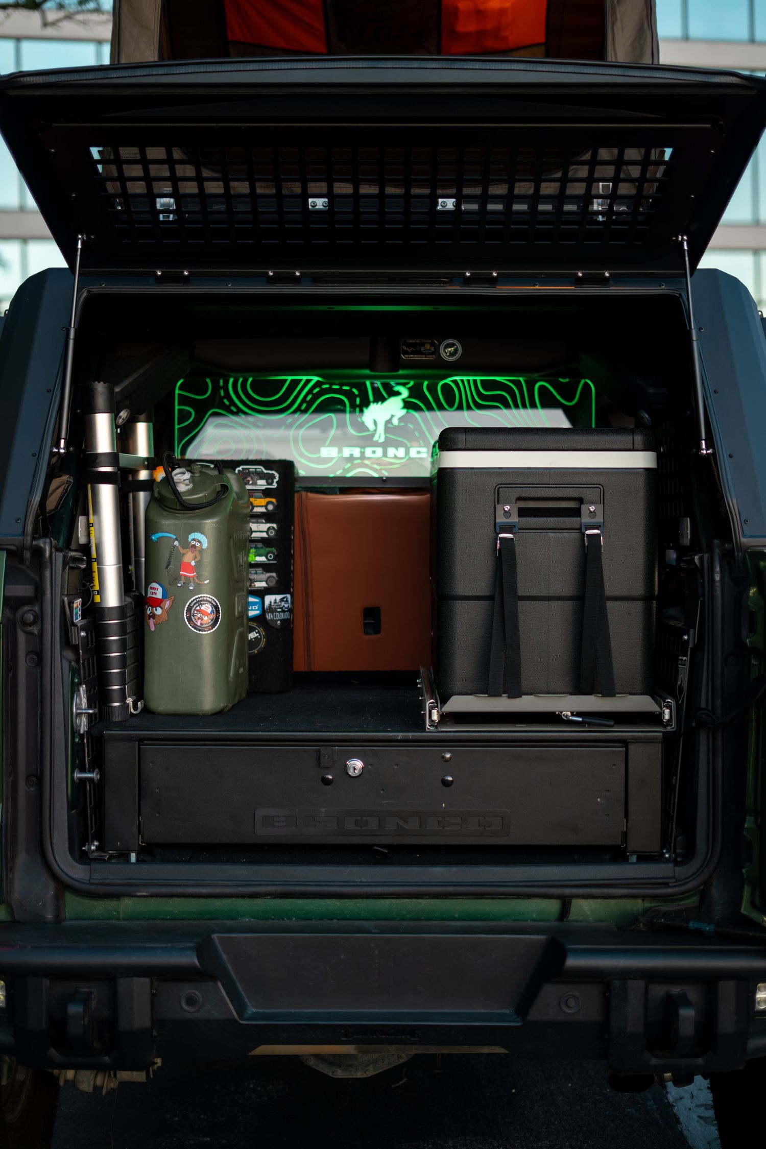 Organized storage compartment in vehicle trunk showing coolers and camping gear with green ambient lighting.