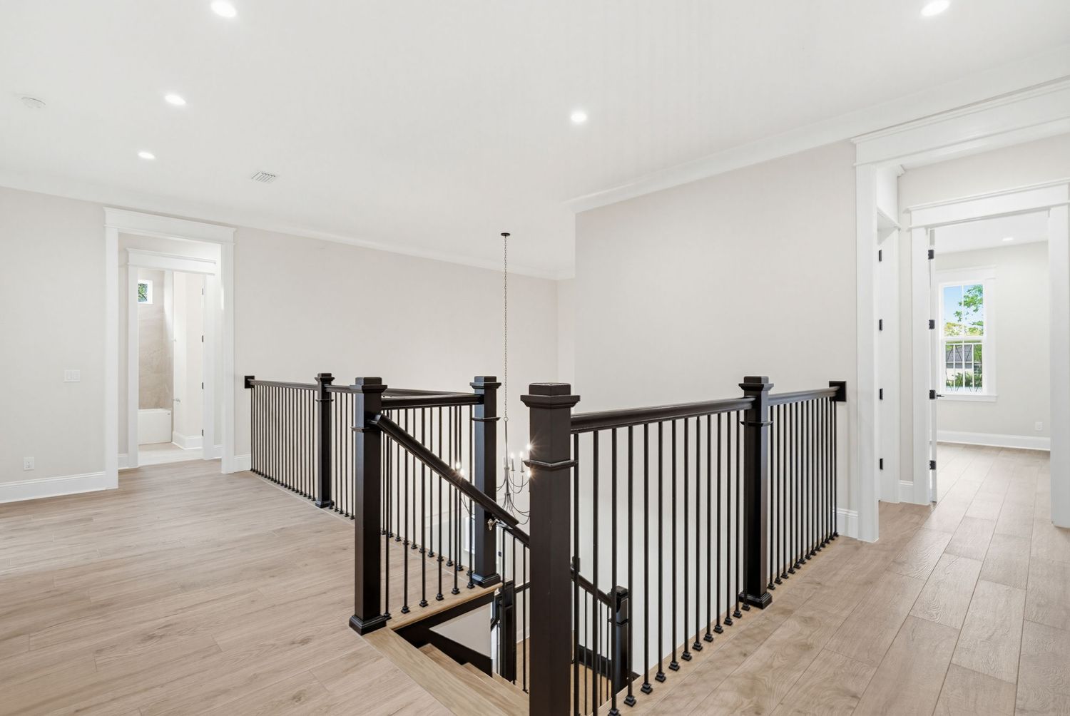 Modern white hallway with black metal staircase railing and light hardwood floors showcases contemporary interior design.