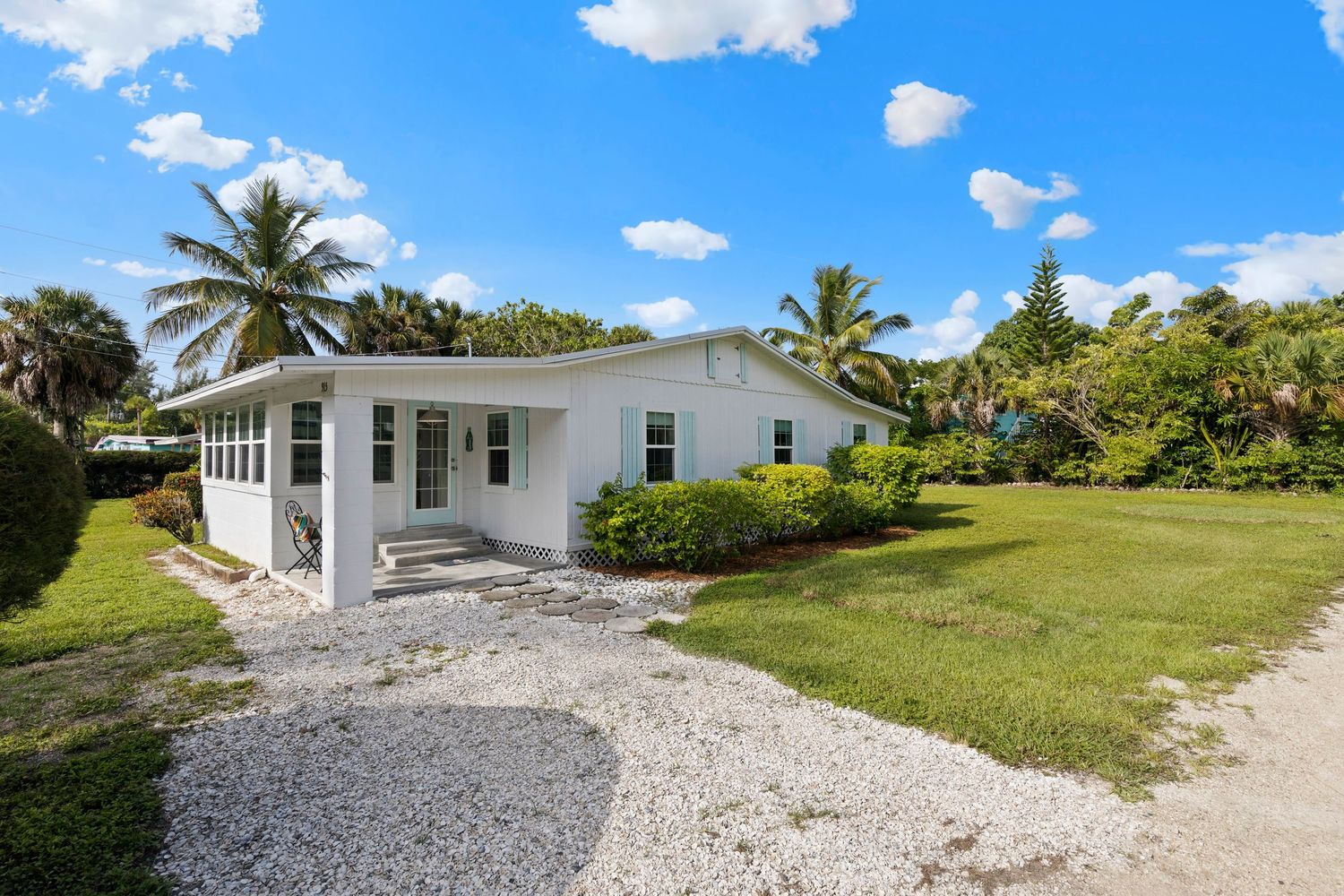 Aerial view of a white coastal residence with palm trees and shell driveway surrounded by lush greenery.