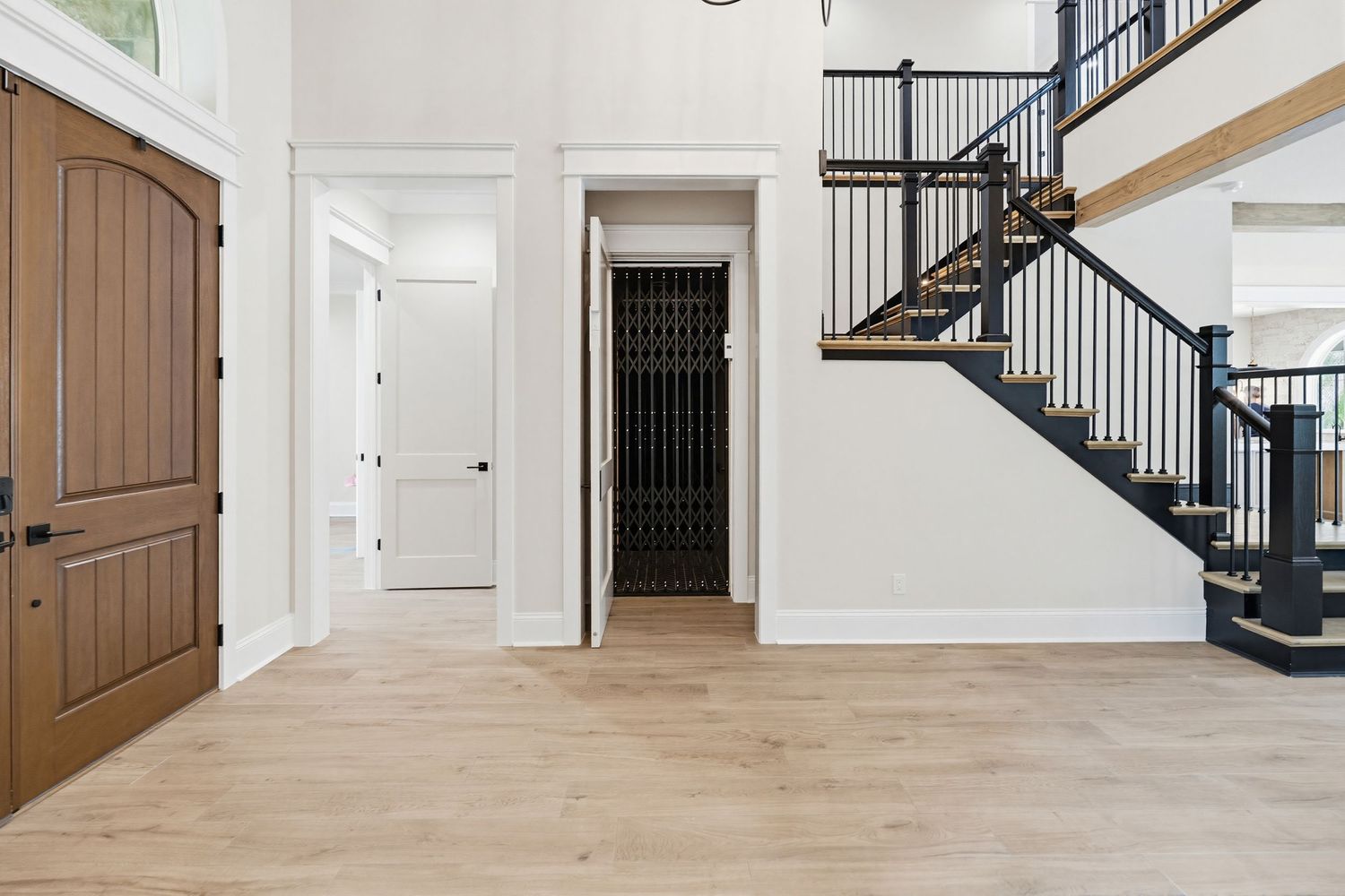 Modern white and brown staircase with black metal railing in a bright residential foyer with hardwood floors.