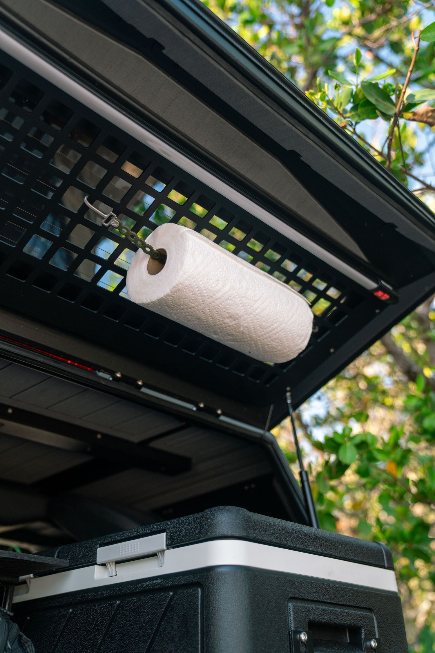 Overhead storage rack system in a vehicle showing paper towel roll mounted underneath.