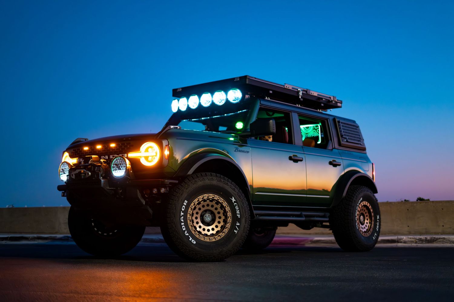Modified off-road vehicle silhouetted against blue sky with light bar illuminated at dusk.