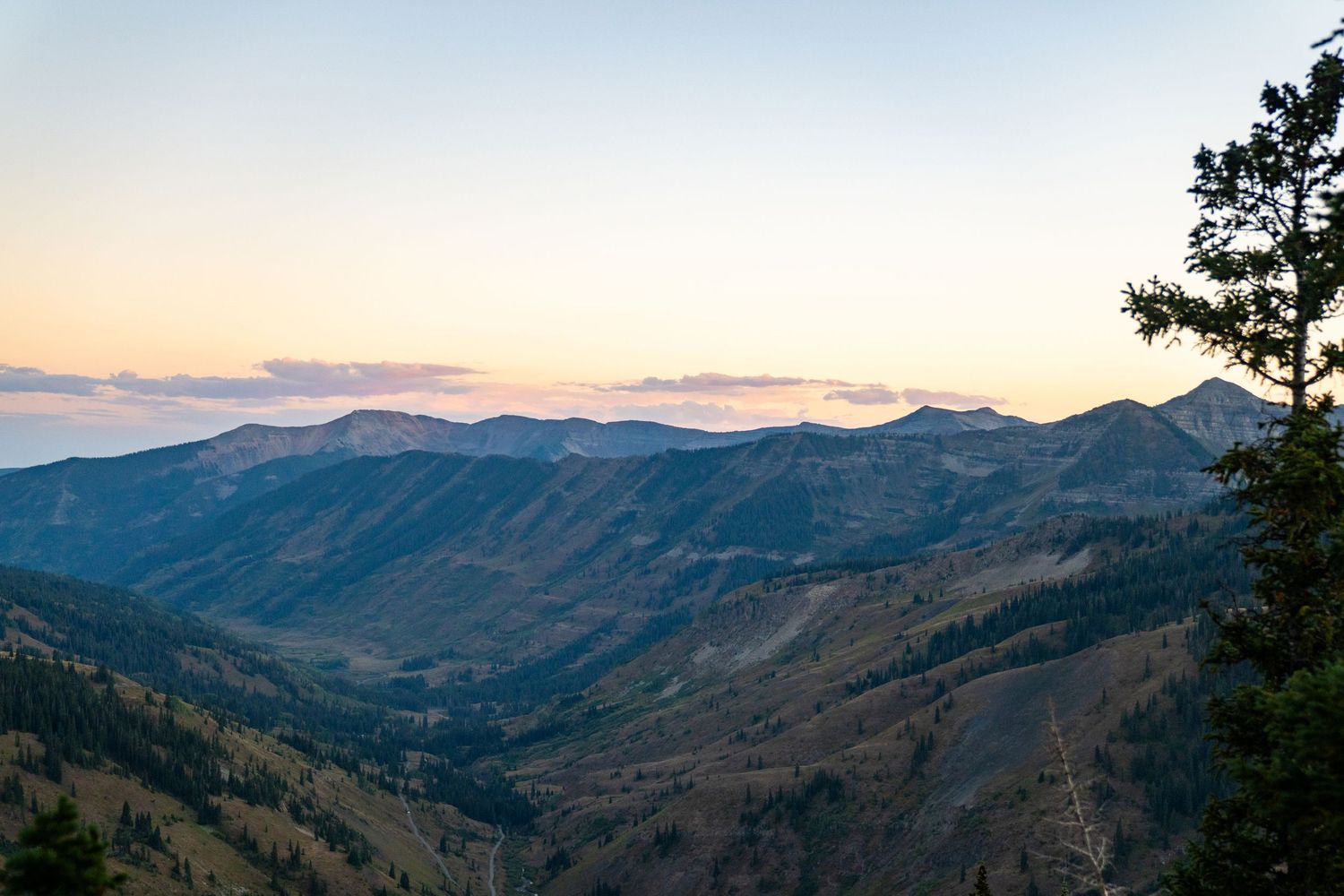 Sunset view over mountainous valley with layered ridges fading into the distance.