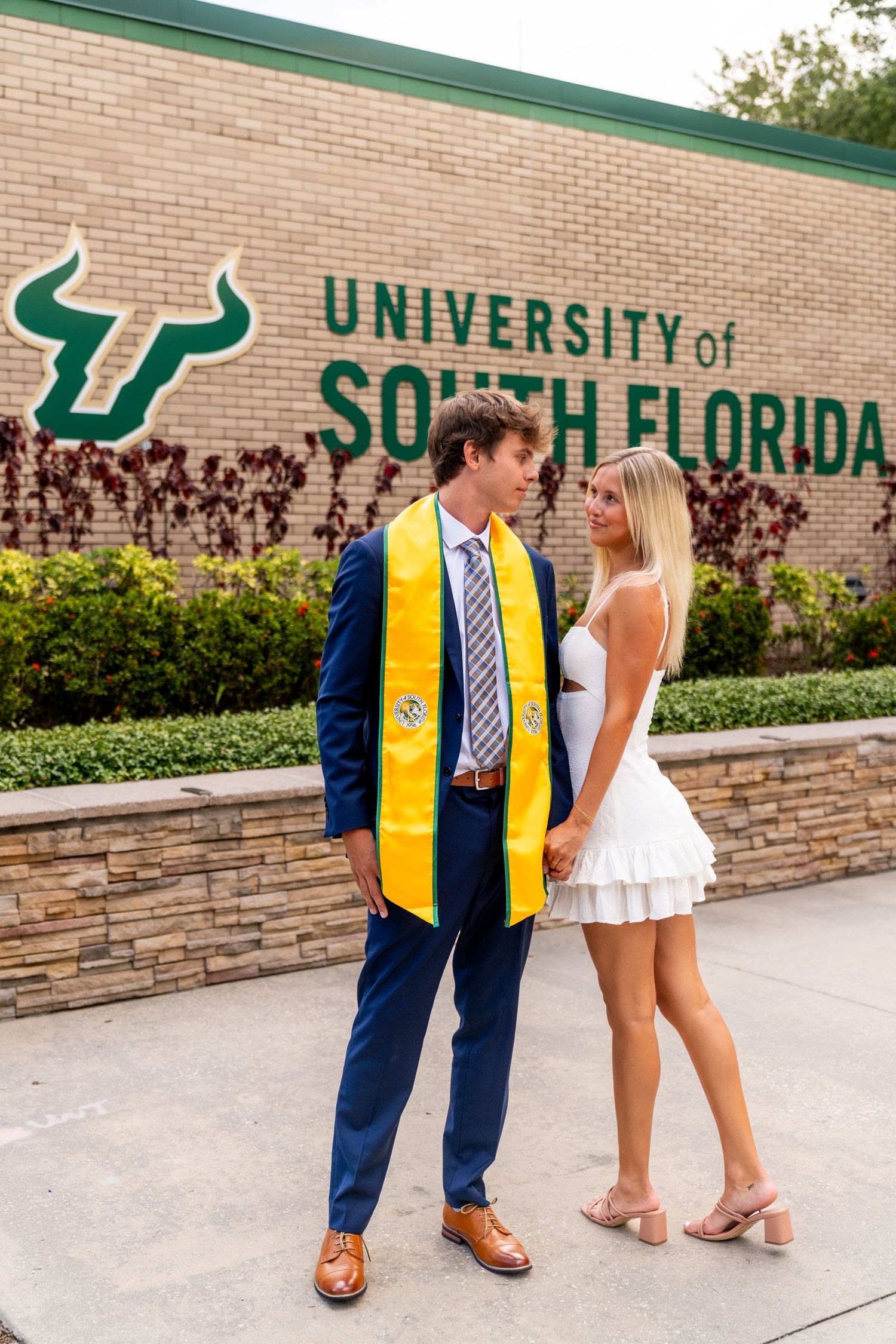 A graduation photoshoot at the University of South Florida campus with brick walls and signage in the background.