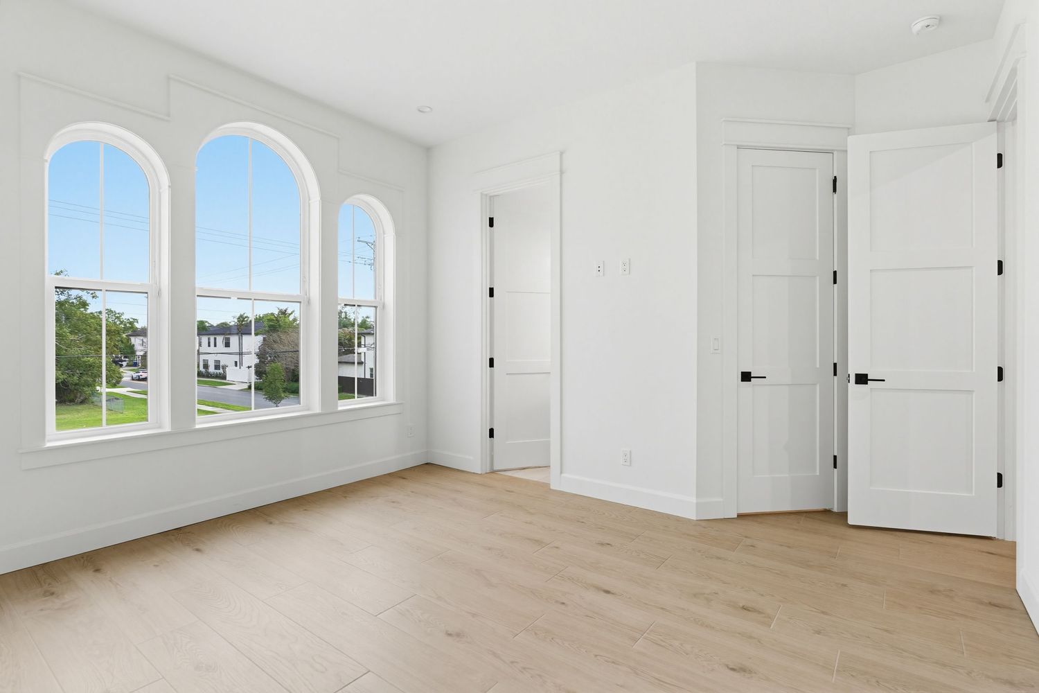 Bright modern bedroom with arched windows, light hardwood floors, and white walls showcasing an open, airy design.