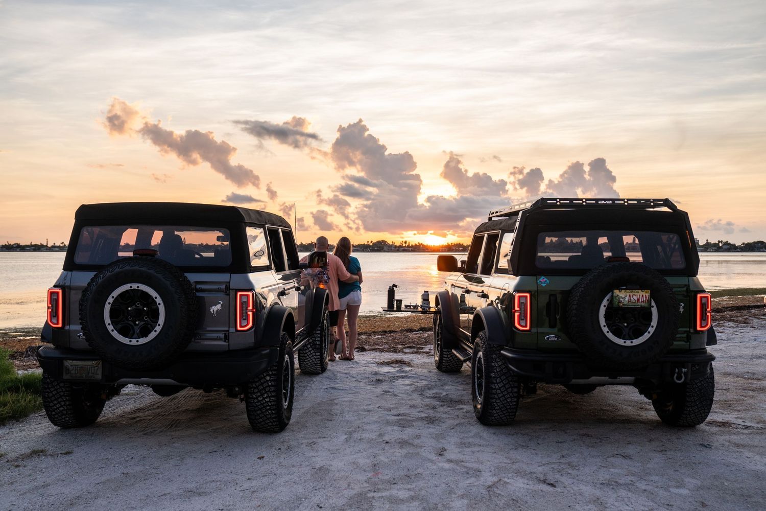 Silhouettes of pickup trucks against dramatic sunset sky at beach.