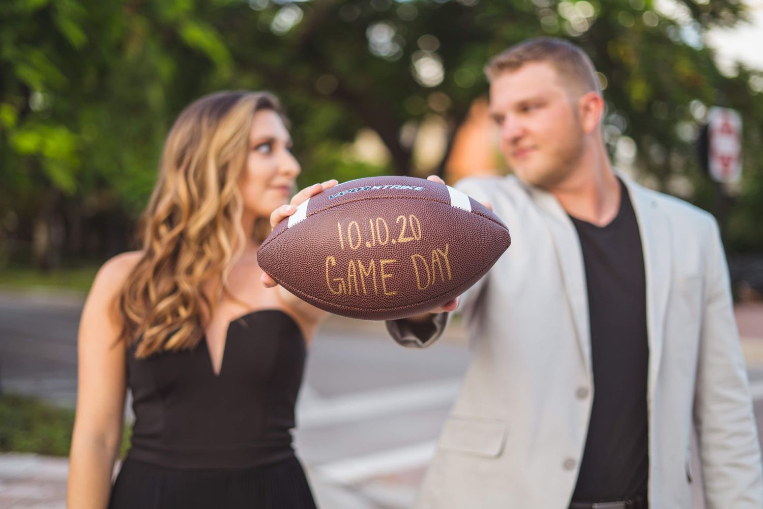 Romantic engagement photos with couple holding football in outdoor setting.