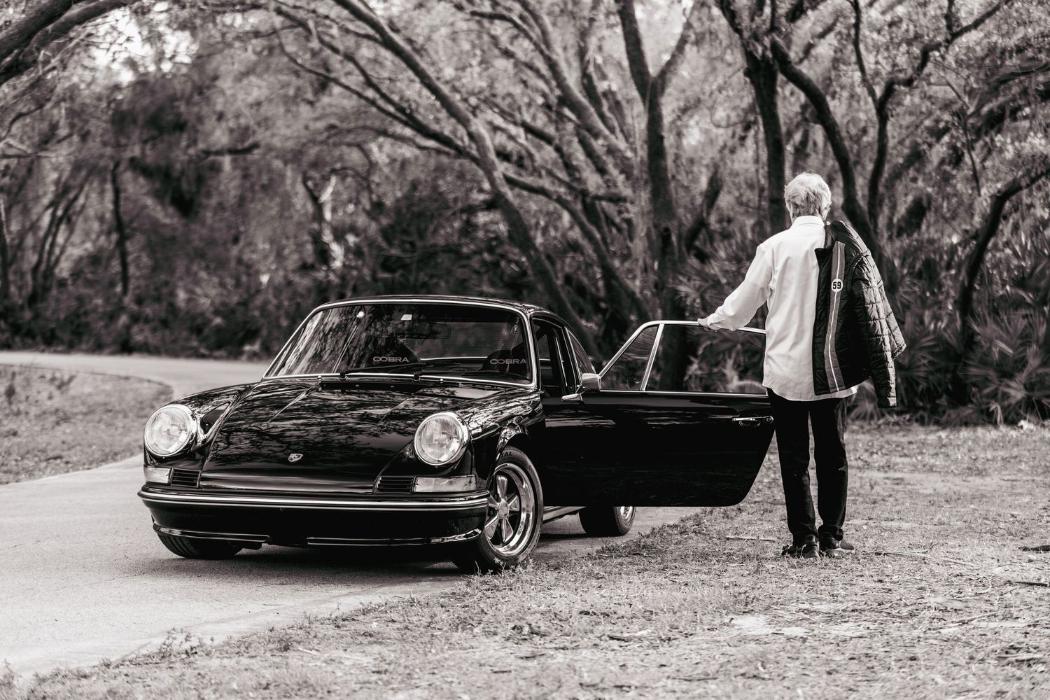 A black vintage car parked on a tree-lined road during a photoshoot.