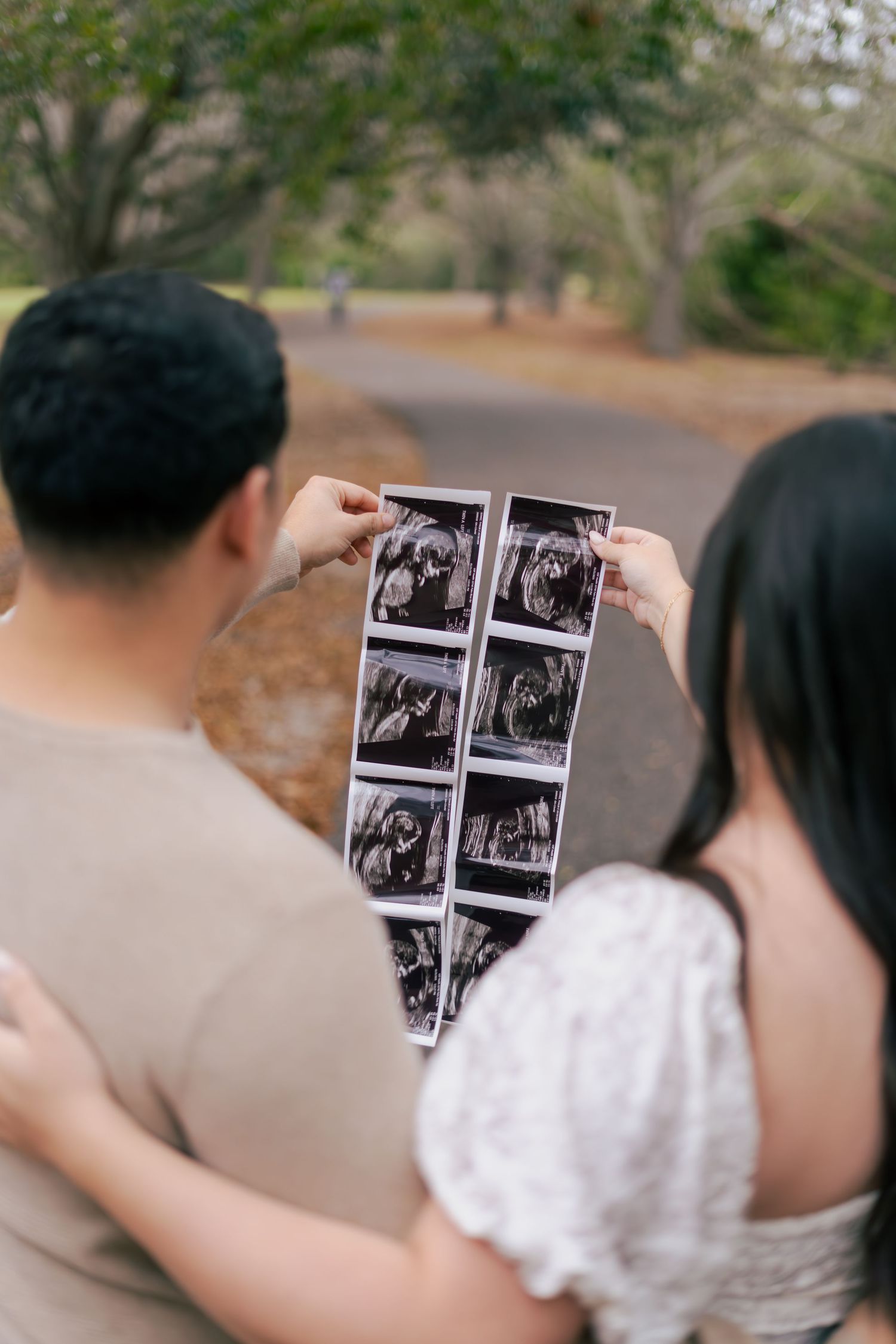 Hands hold up black and white ultrasound photos against a blurred outdoor background.