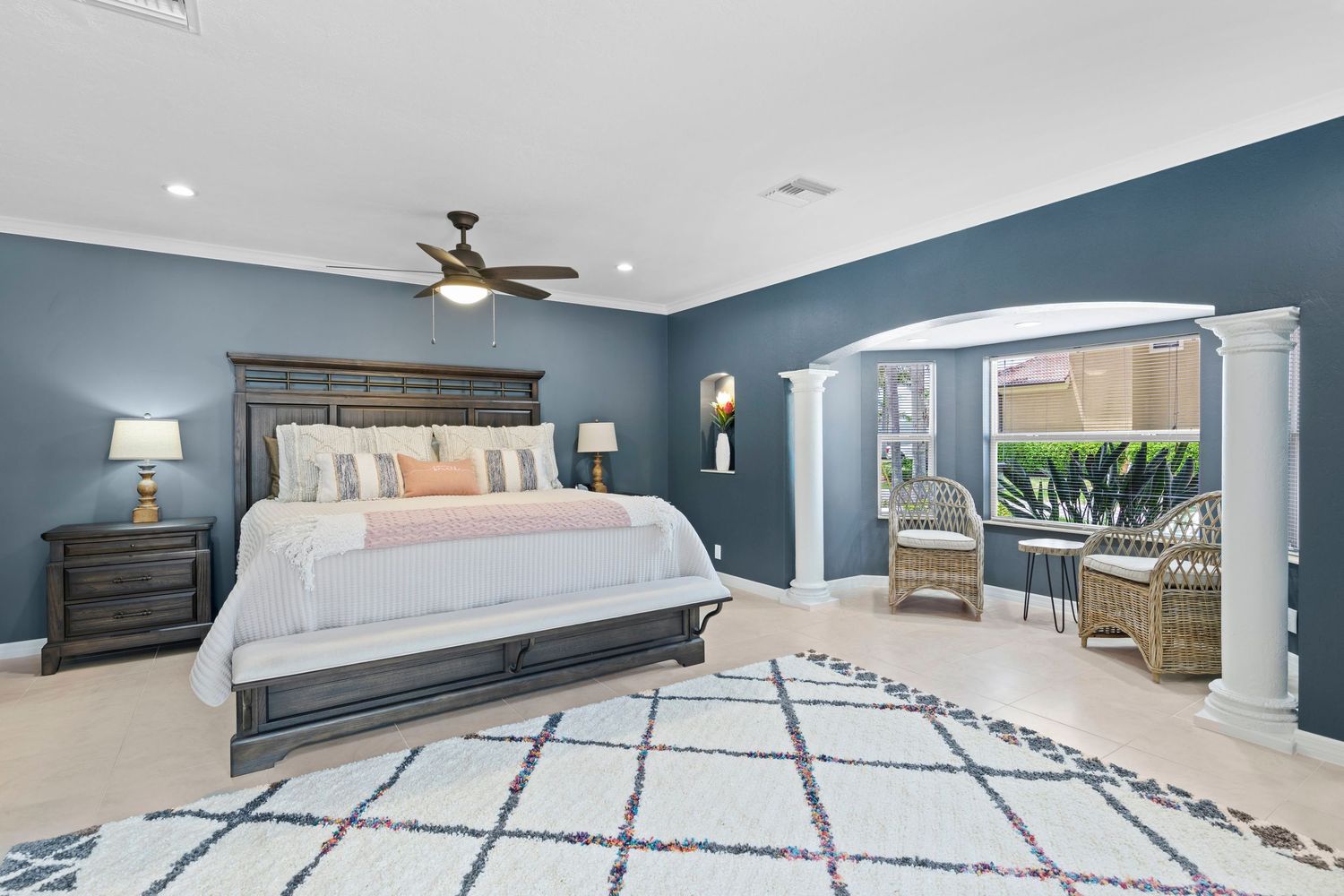 Spacious master bedroom with blue walls, white bedding, geometric rug, and adjoining sitting area through arched doorway.