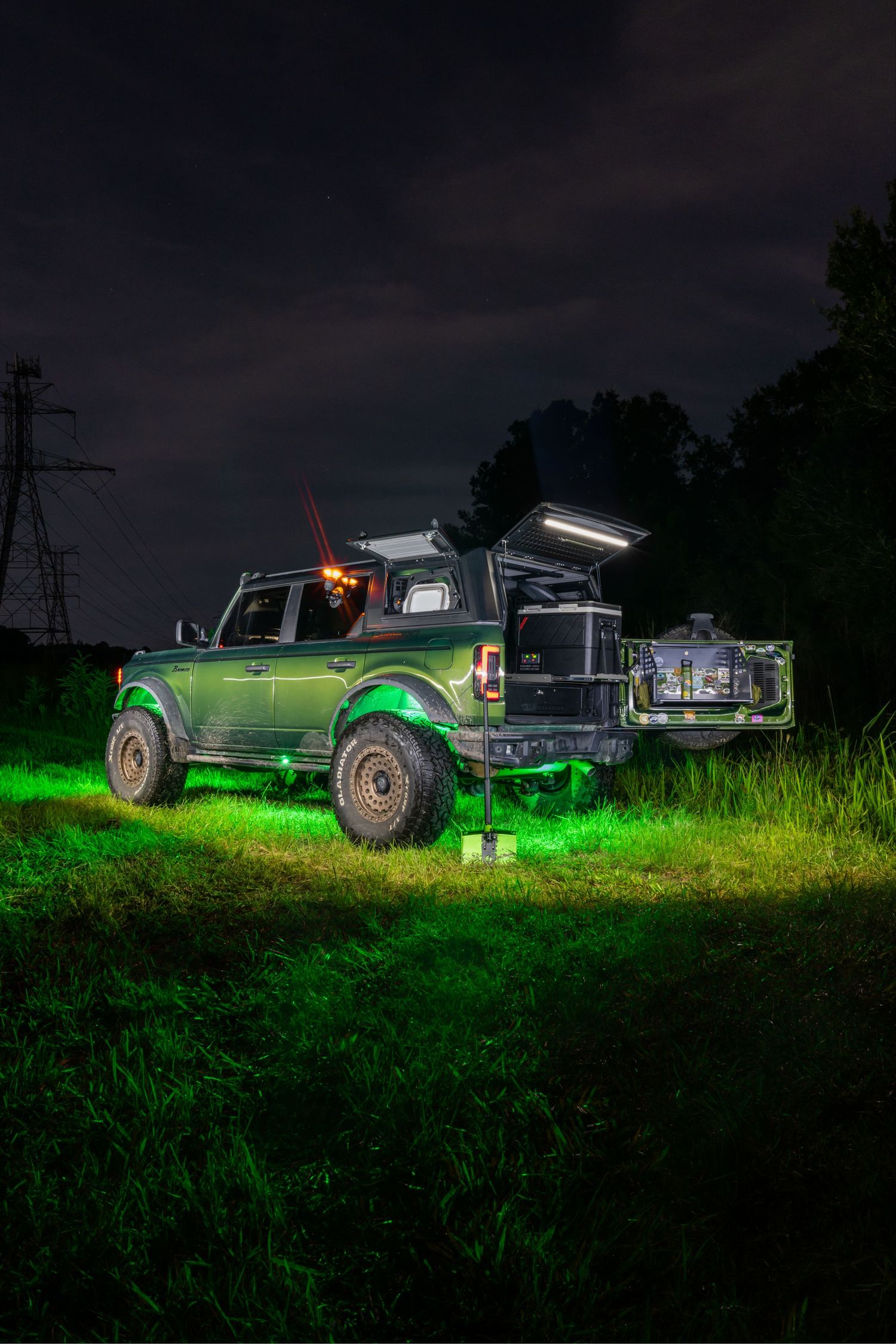 Modified truck illuminated by green lighting in nighttime field setting.