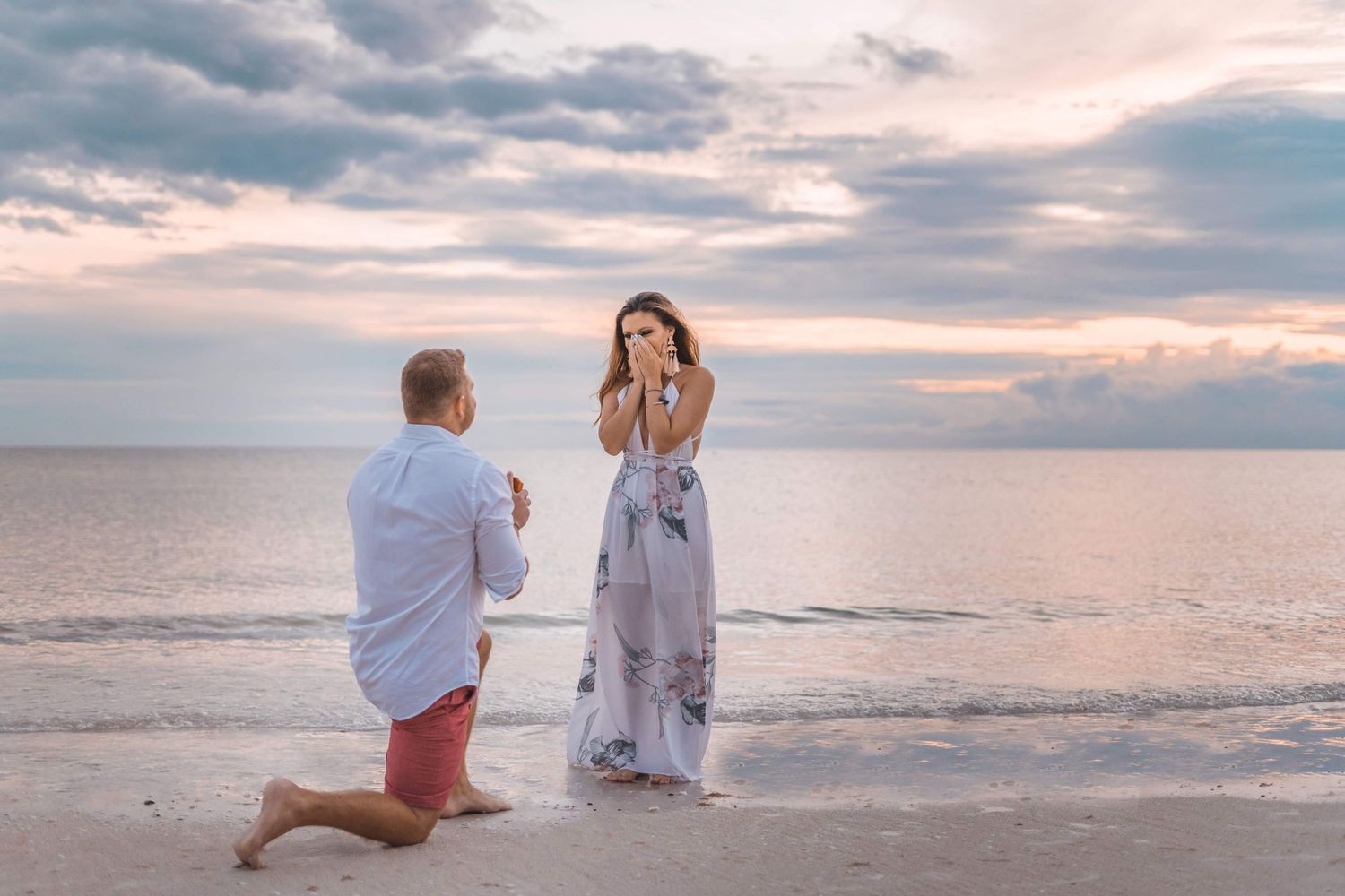 Beach proposal at sunset with dramatic cloudy sky over the ocean.