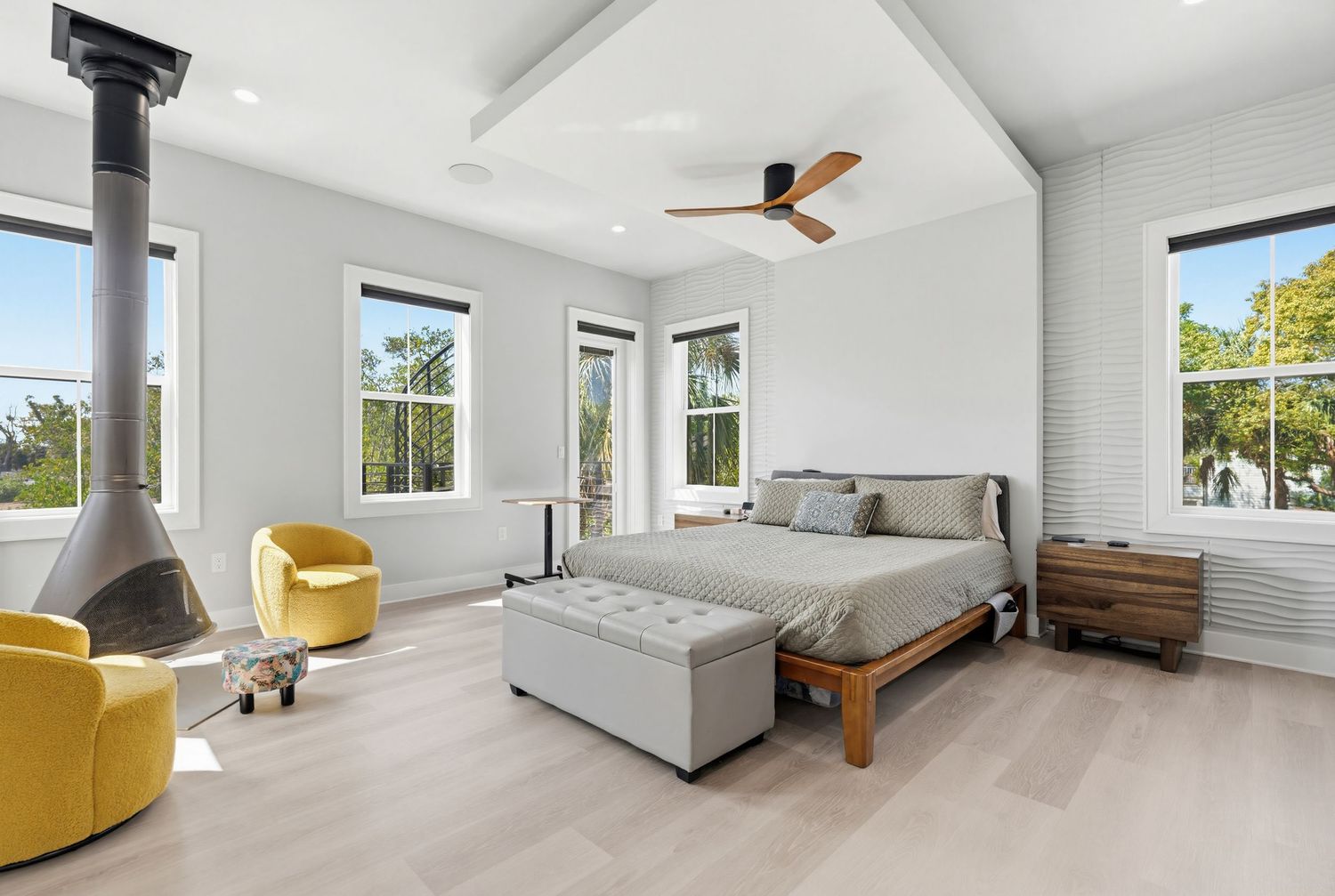 Bright white bedroom with ceiling fan, hardwood floors, and large windows offering natural light.