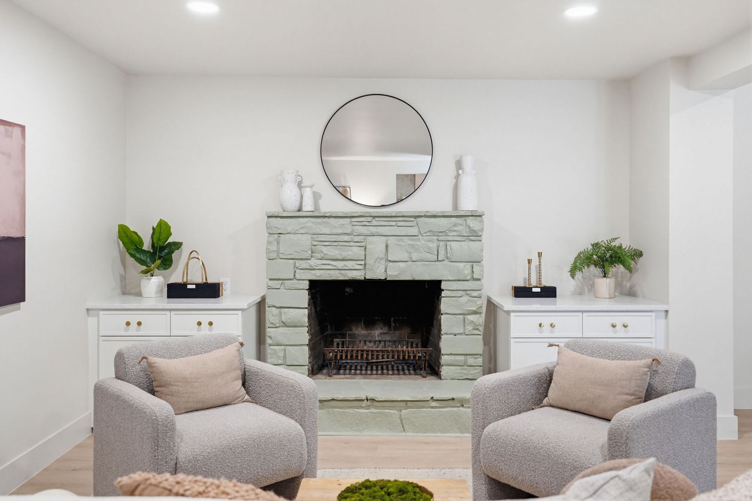 Modern white living room with grey sofa, round mirror, and potted plants showcasing a minimalist Scandinavian design style.
