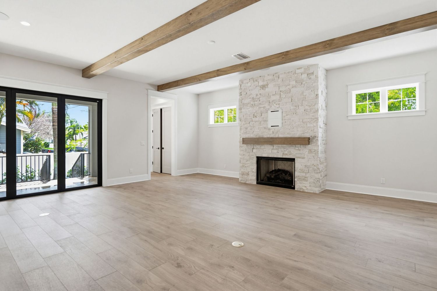 Modern open concept living room with exposed wooden beams, light hardwood floors, and stone accent wall.