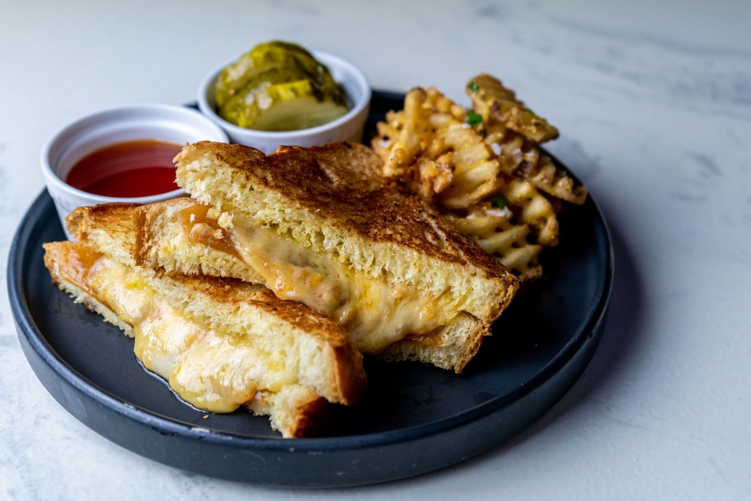 Golden crispy phyllo pastries filled with cheese and served with dipping sauces on dark plates against marble surface.