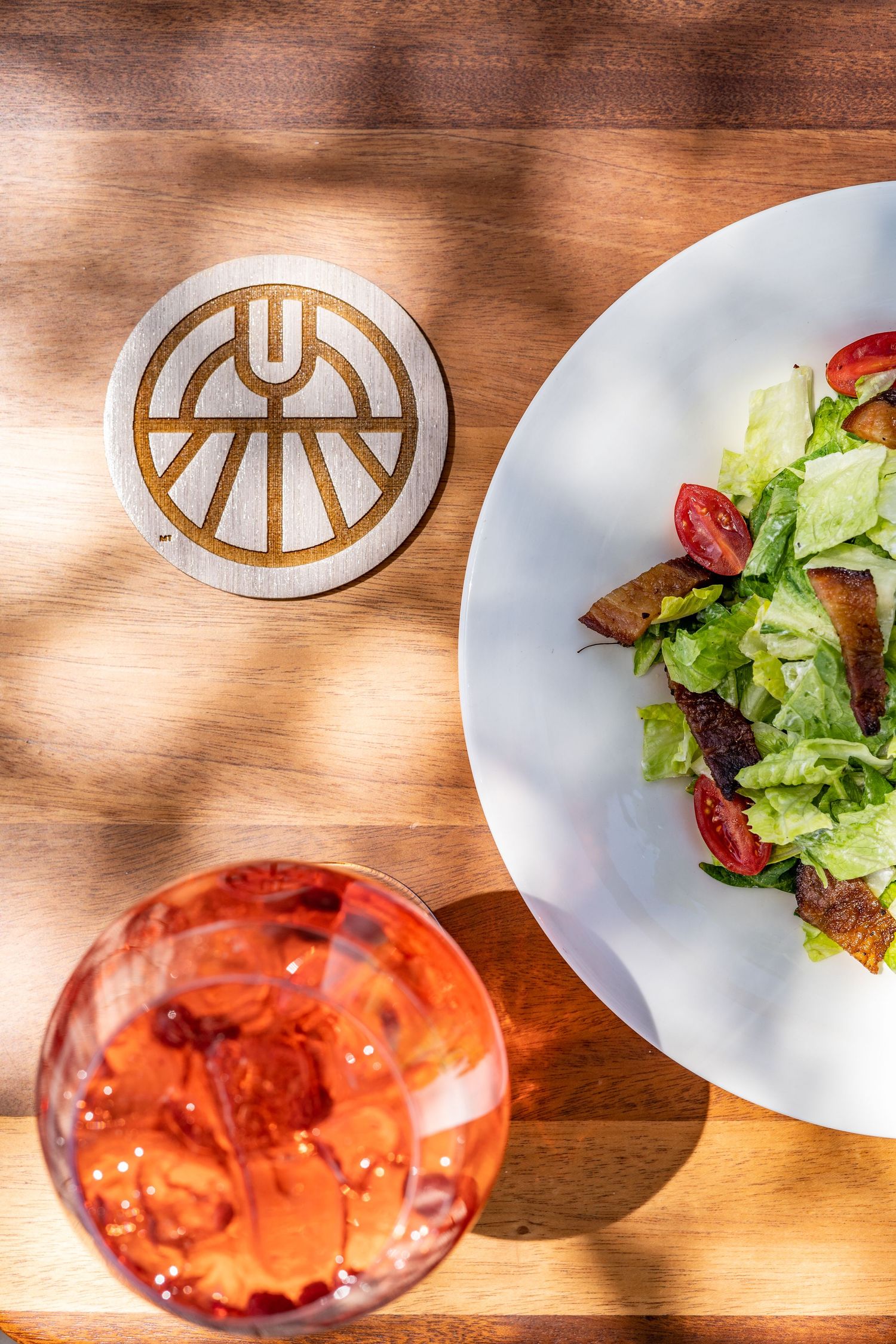 Sequence of plated salads and drinks on a wooden table with natural lighting.