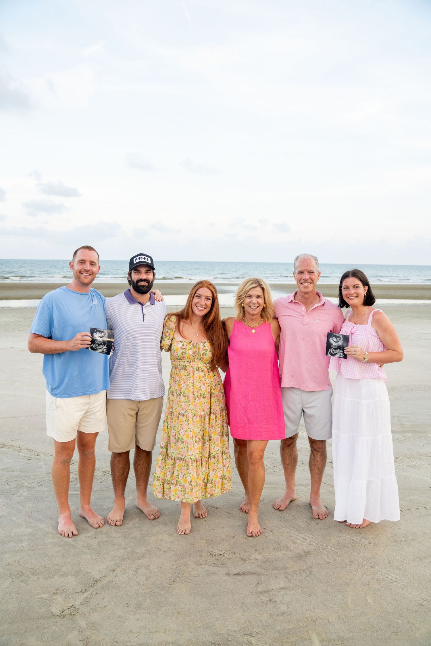 A family group poses together on a sandy beach with the ocean visible in the background.