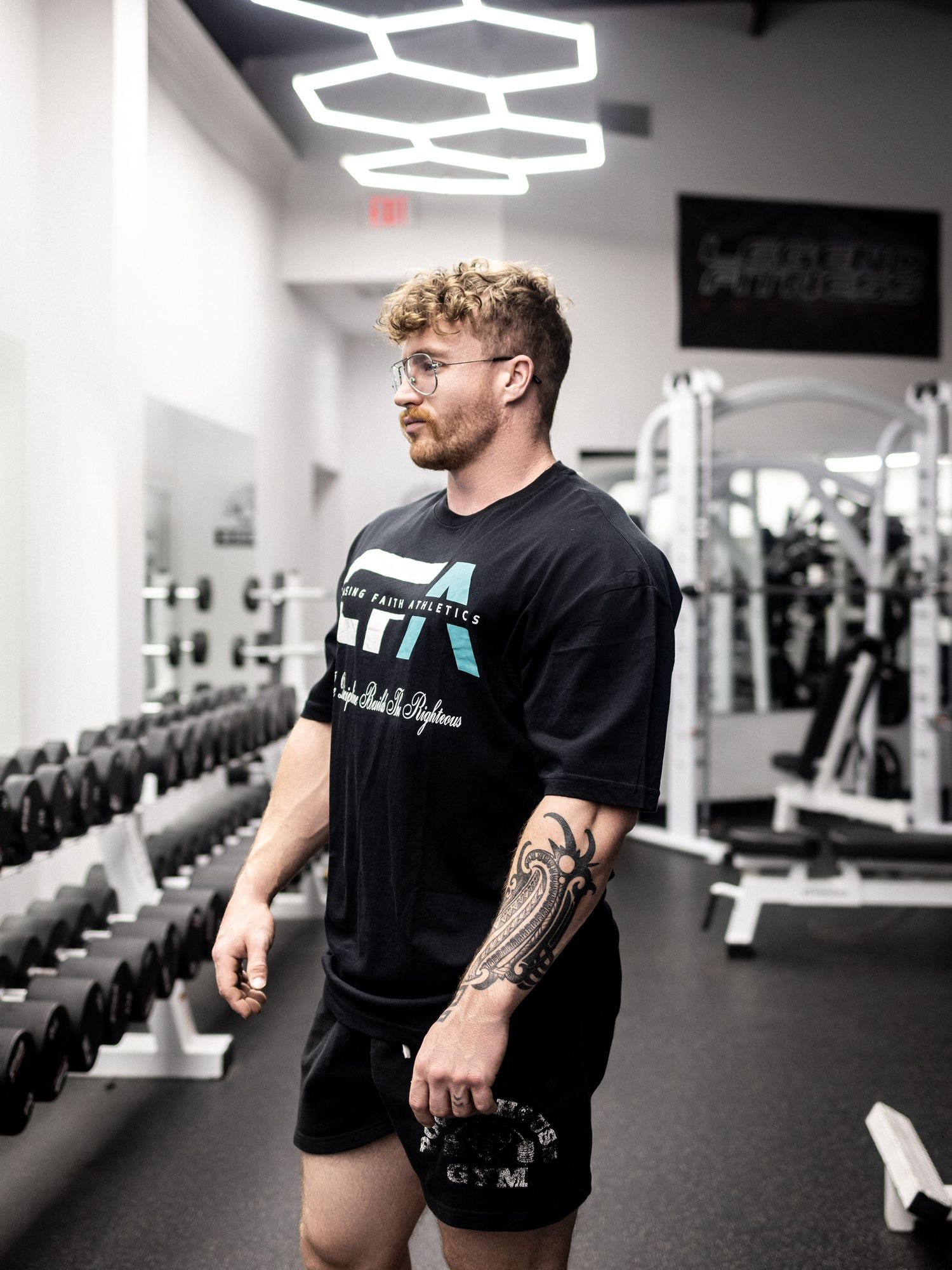 Athletic trainer in black t-shirt demonstrates proper form in modern fitness facility with hexagonal lighting.