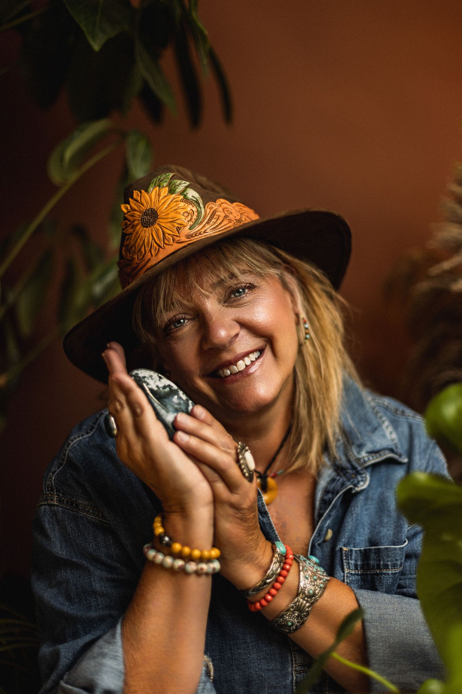 Bohemian style portrait with denim jacket, decorated hat, and colorful jewelry in warm lighting.
