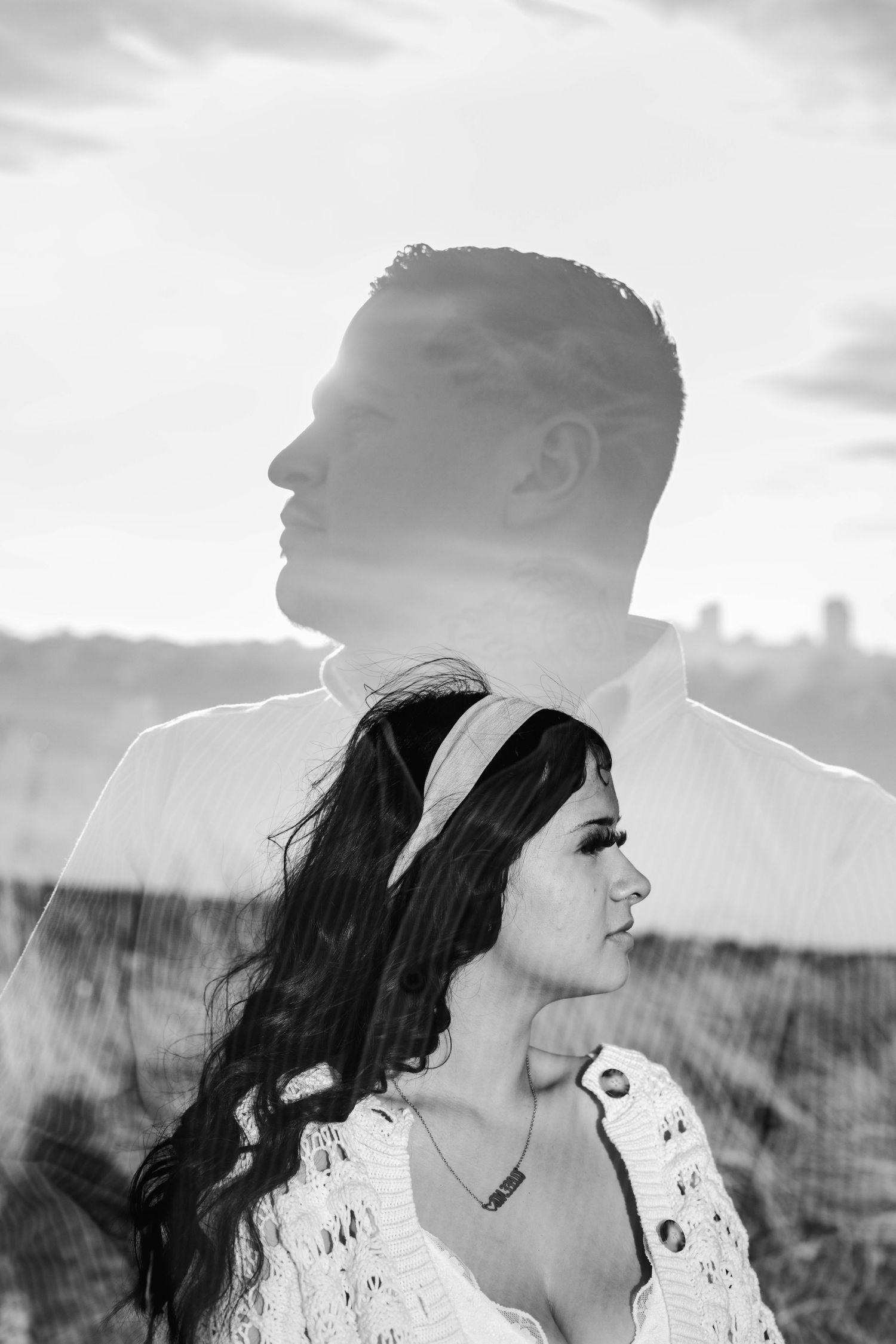 Black and white double exposure portrait of a couple, woman in foreground with long dark hair, man's profile overlaid behind her.