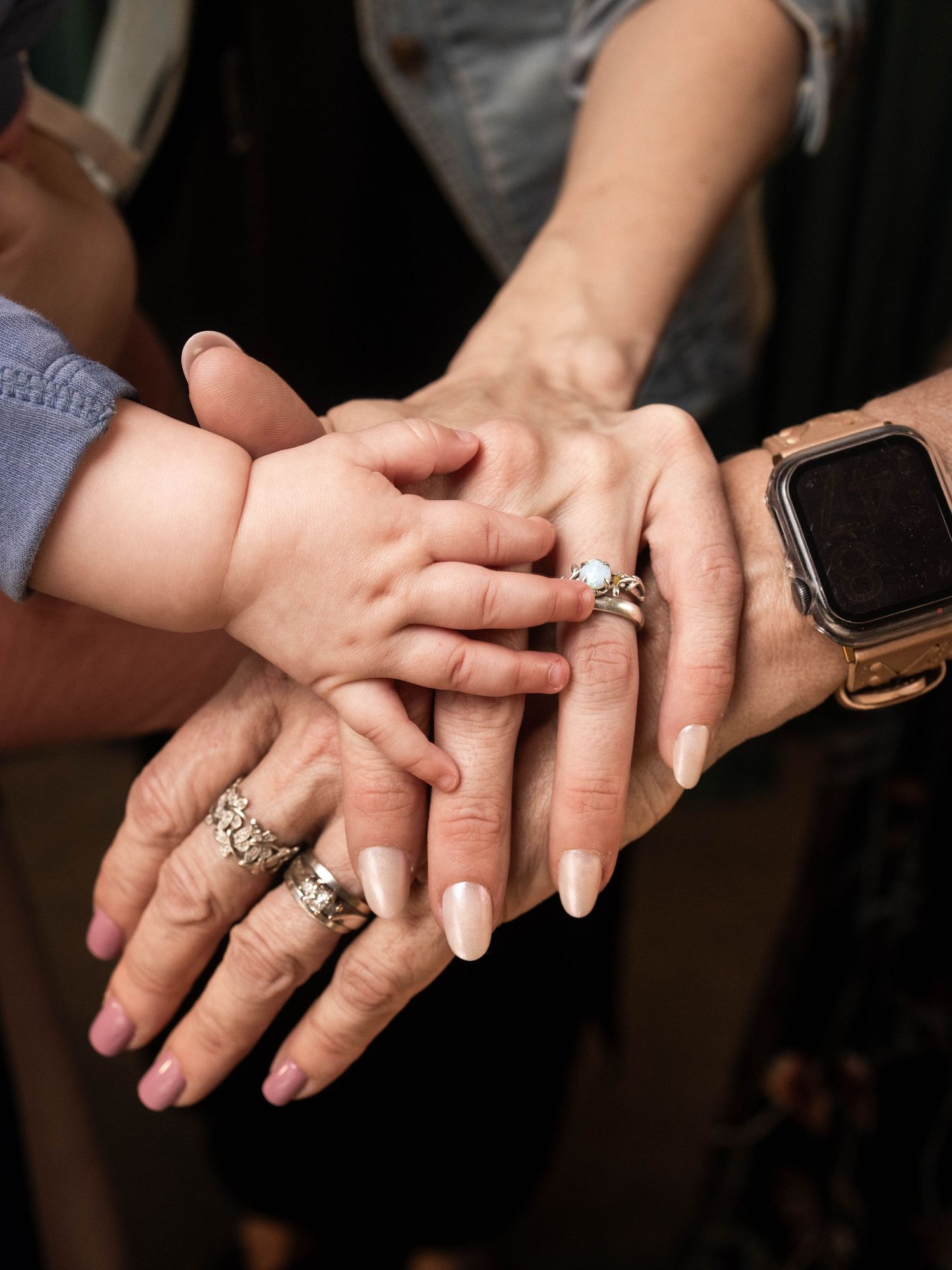Multiple generations of hands stacked together, featuring rings, manicured nails, and a smartwatch, symbolizing family unity.