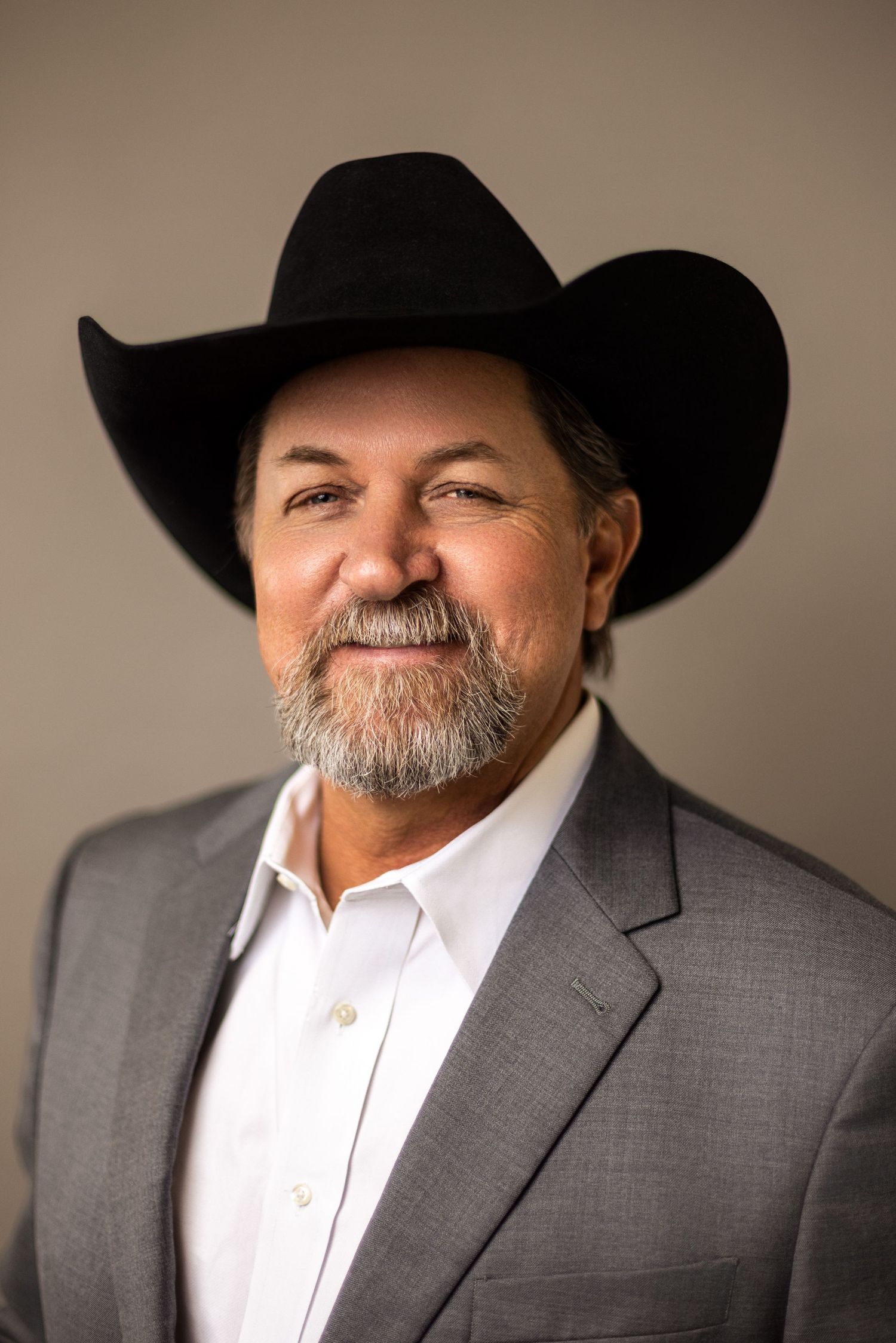 Professional headshot of person in black cowboy hat and gray suit against neutral background.