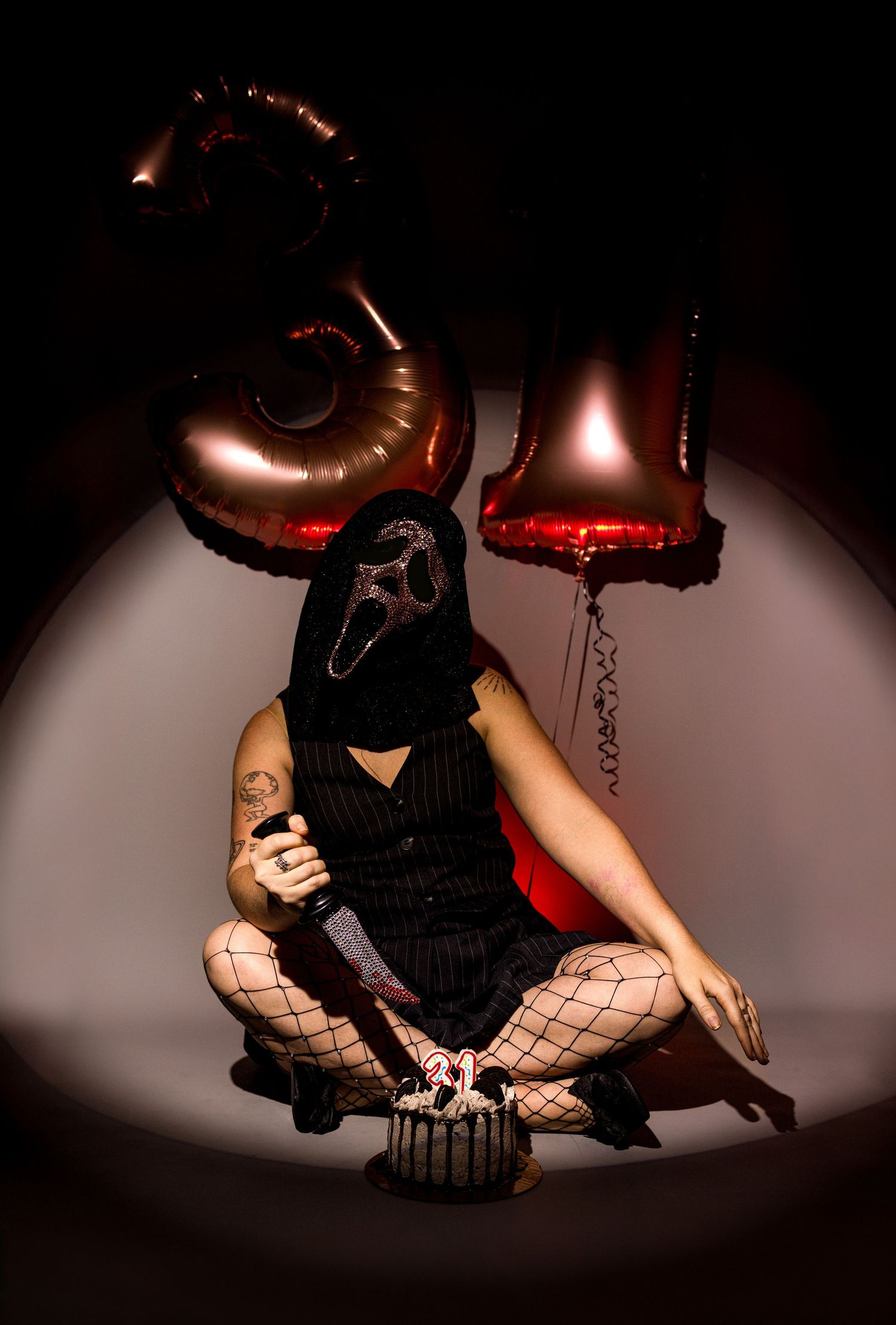 Person in Ghostface mask sitting with balloons shaped as 31 for Halloween celebration.