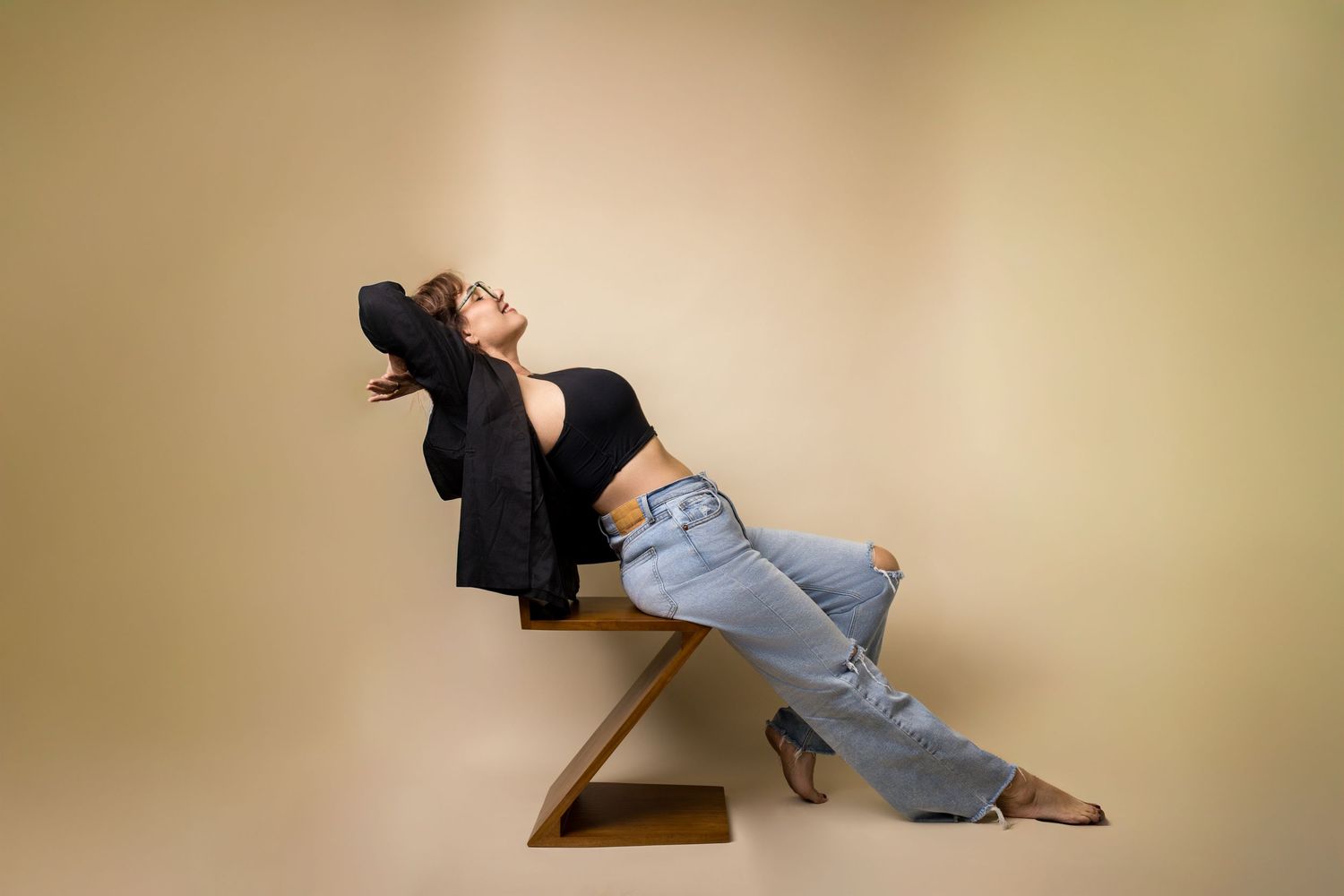 Person in black top and jeans lying on wooden stairs in artistic poses against beige background.