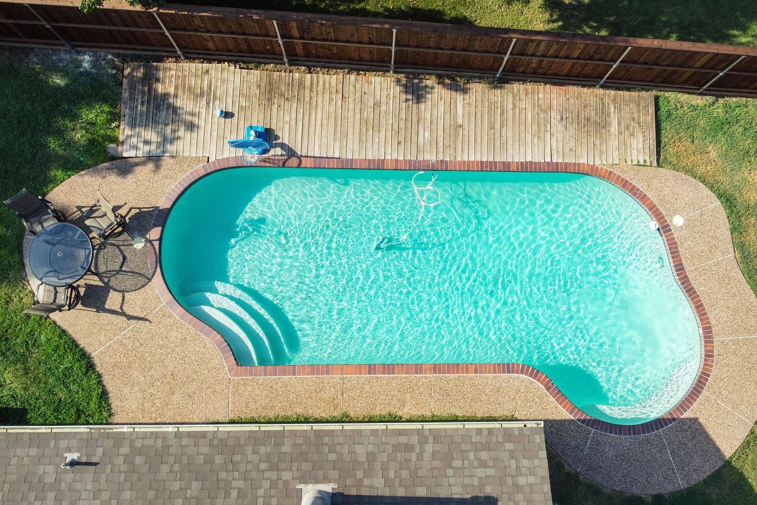 Aerial view of a rectangular backyard swimming pool with turquoise water, wooden deck, and patio furniture.
