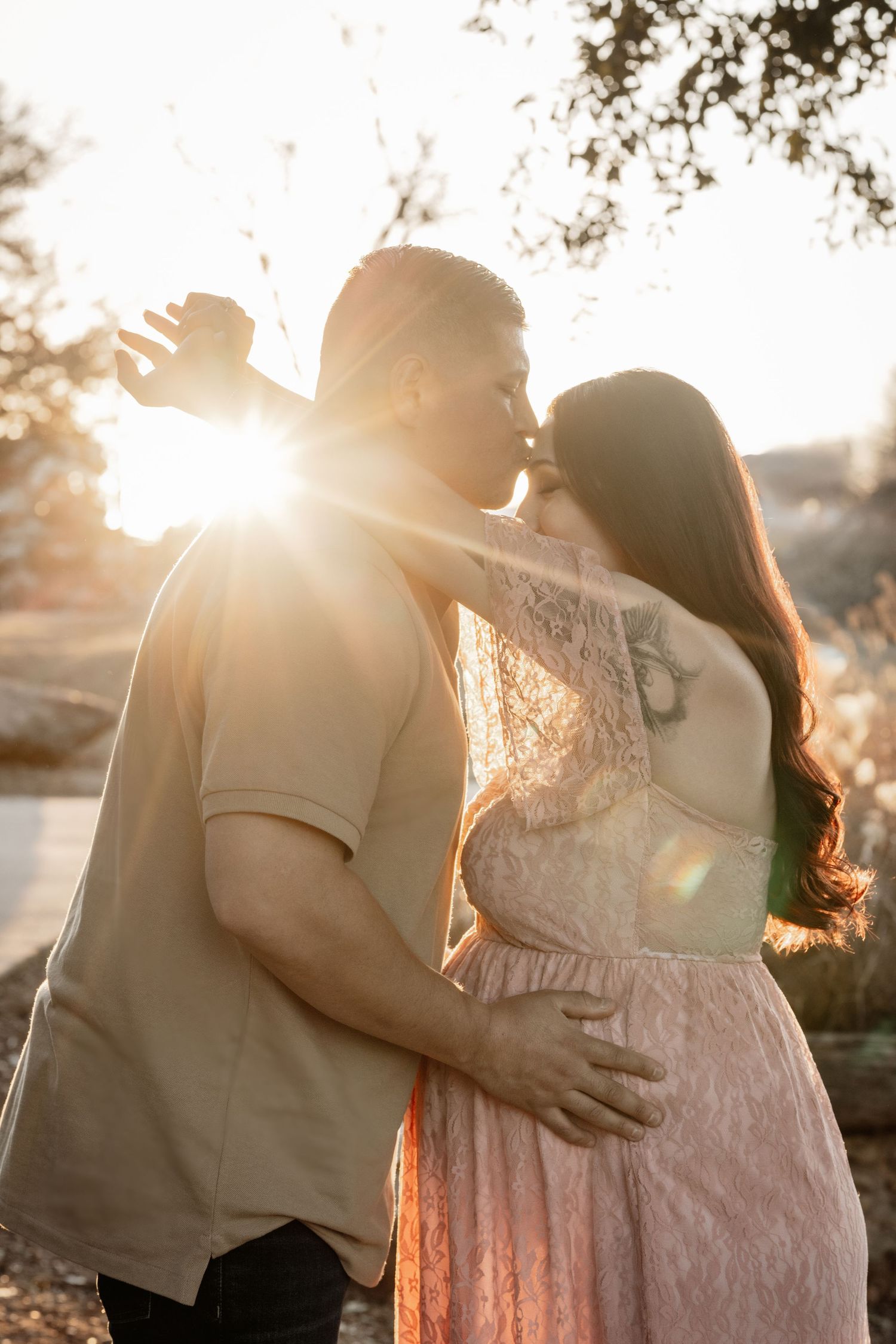 Romantic backlit couple embracing during golden hour with sun flares.