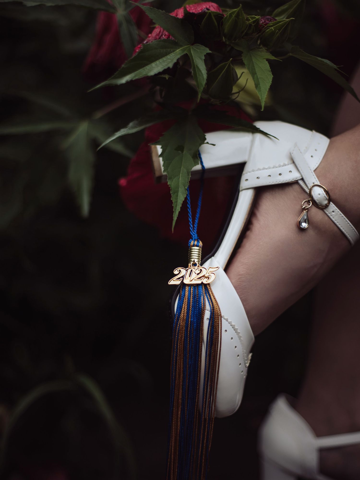 Close-up detail of white shoes with decorative elements against dark floral background.