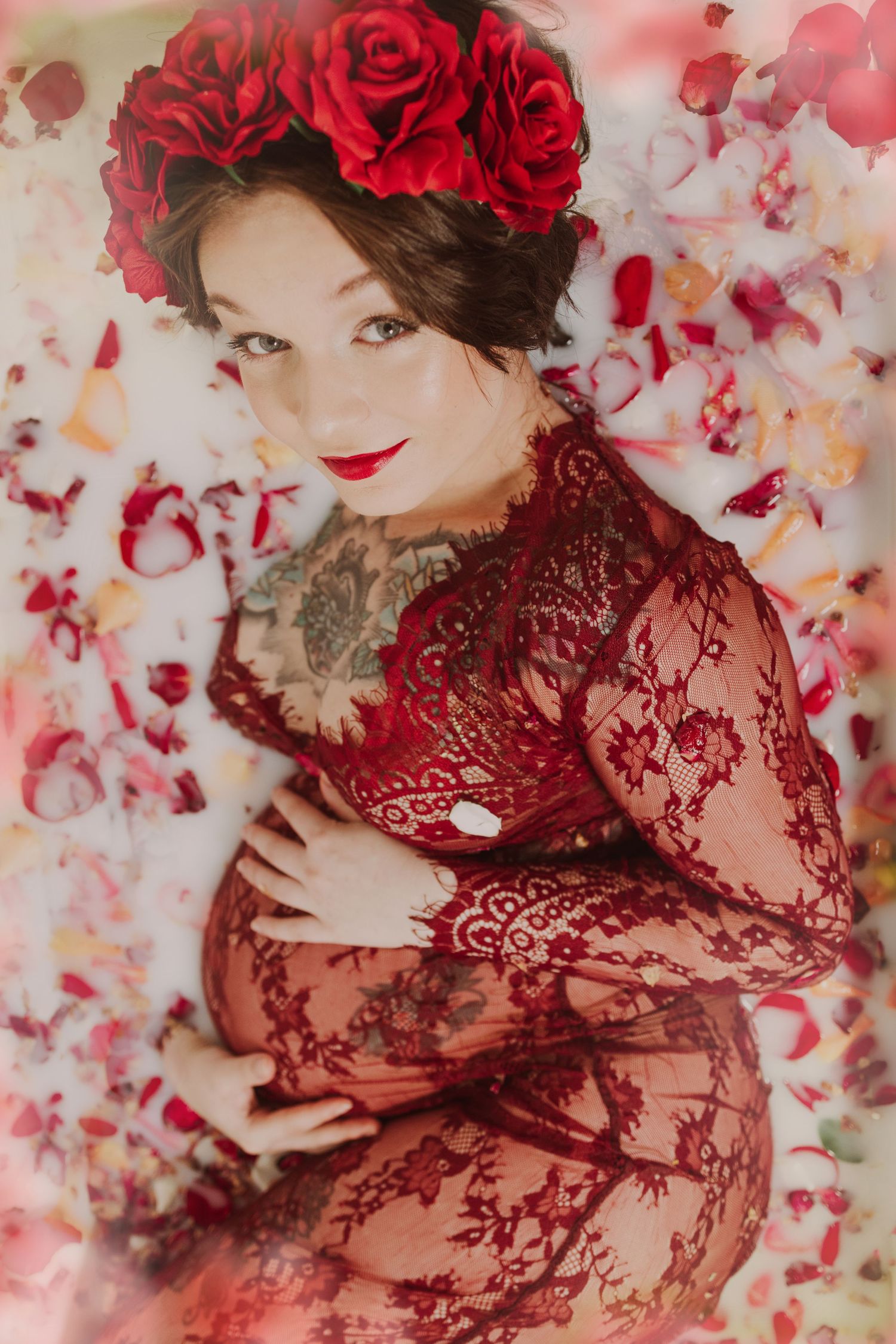 Artistic maternity photo with red roses and lace against floral backdrop.