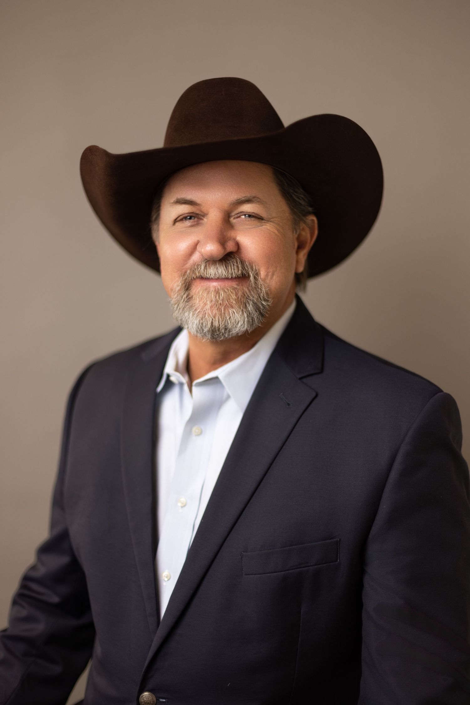 A person in a black suit and cowboy hat poses against a neutral background in a professional portrait series.