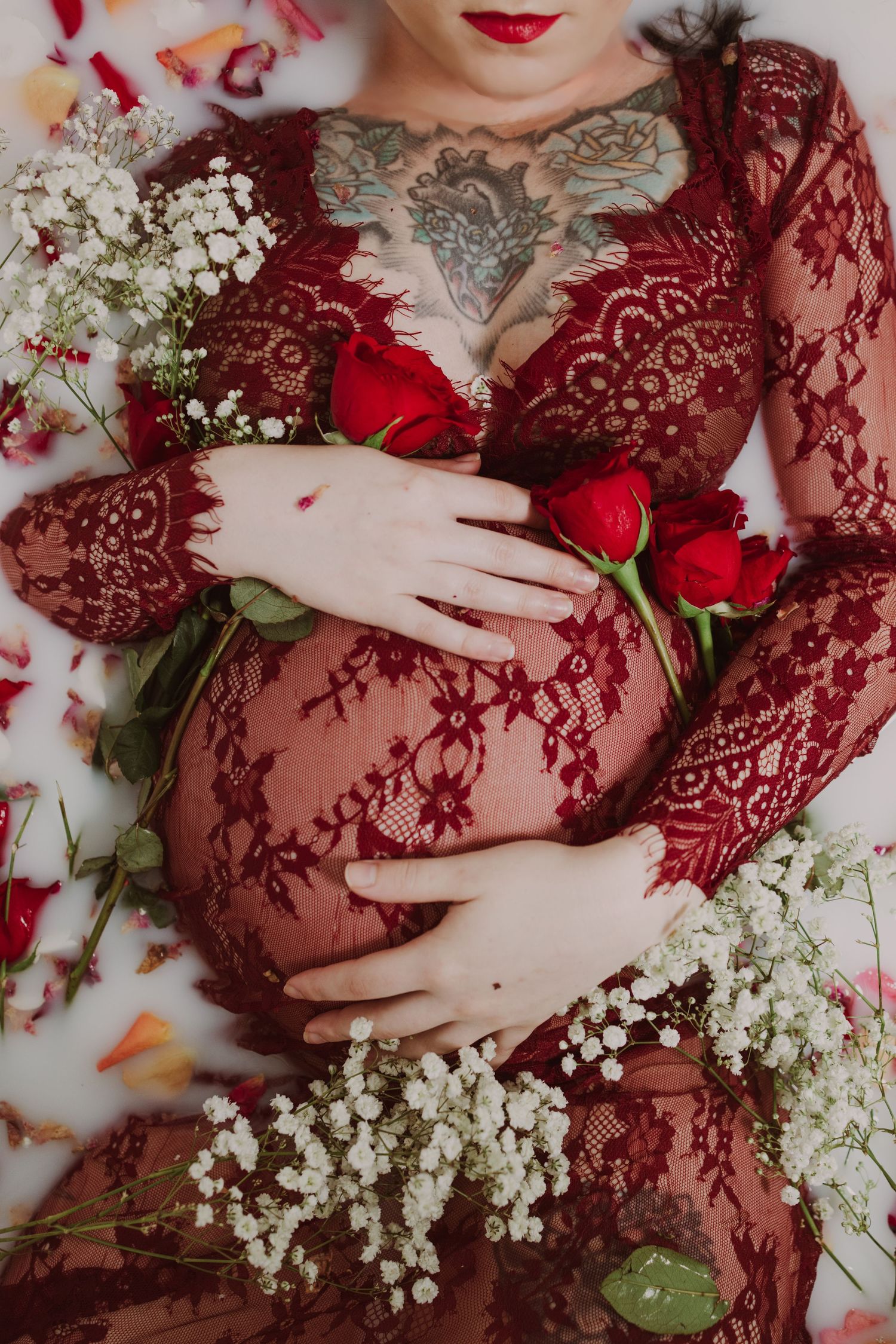 Ethereal maternity photo with red roses, baby's breath flowers, and burgundy lace dress.