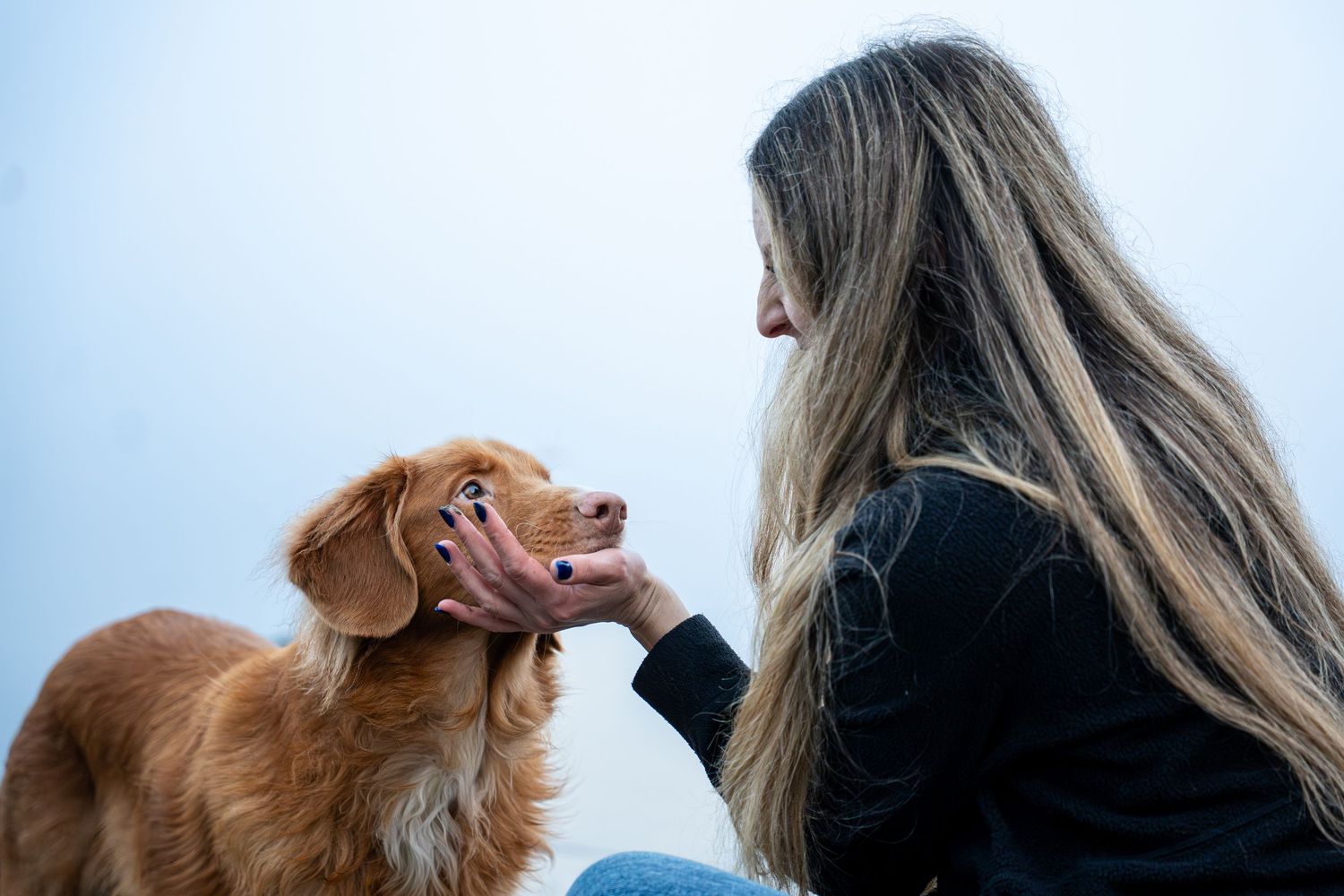 A woman with long hair gently holds the face of a duck toler