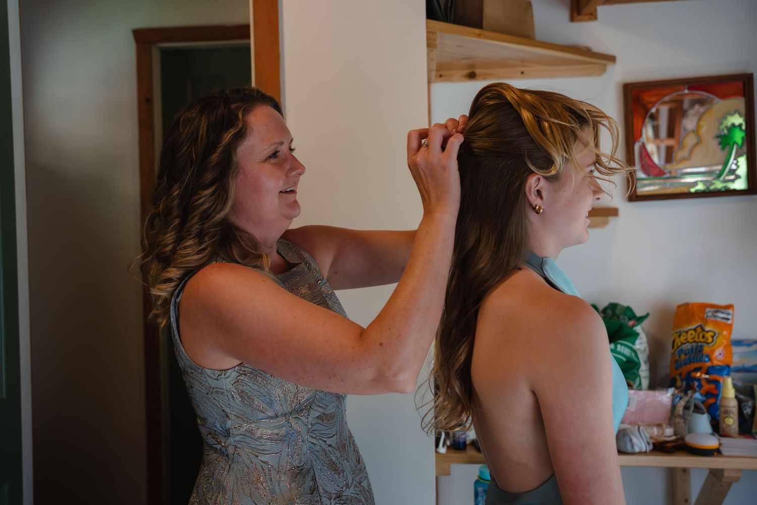 Woman styling another woman's hair indoors, preparing for a special occasion in a bright, cozy room.